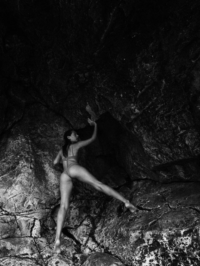 A woman in a swimsuit climbing on a rocky cave wall.