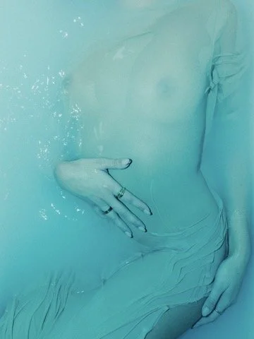 Close-up of a person's torso and hand submerged in water, with the hand resting on their stomach
