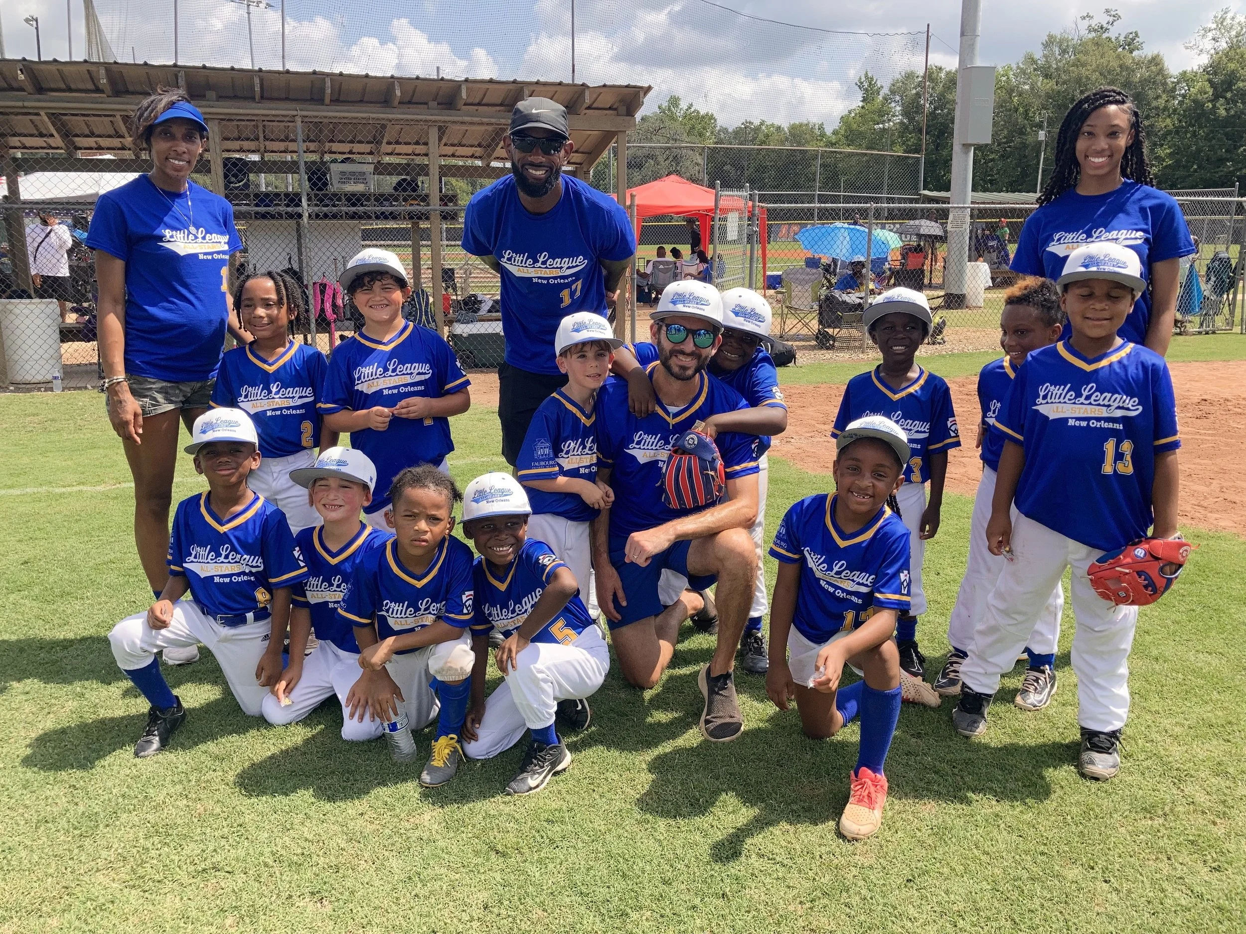 A youth baseball team with coaches and players posing on a baseball field, wearing blue jerseys and white hats, smiling for a group photo.
