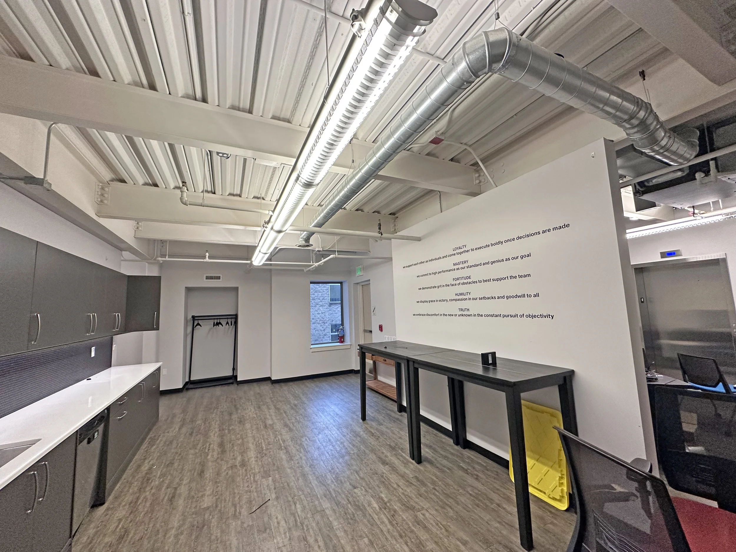 Empty office space with grey cabinets, a small table, chairs, and a wall with motivational quotes.