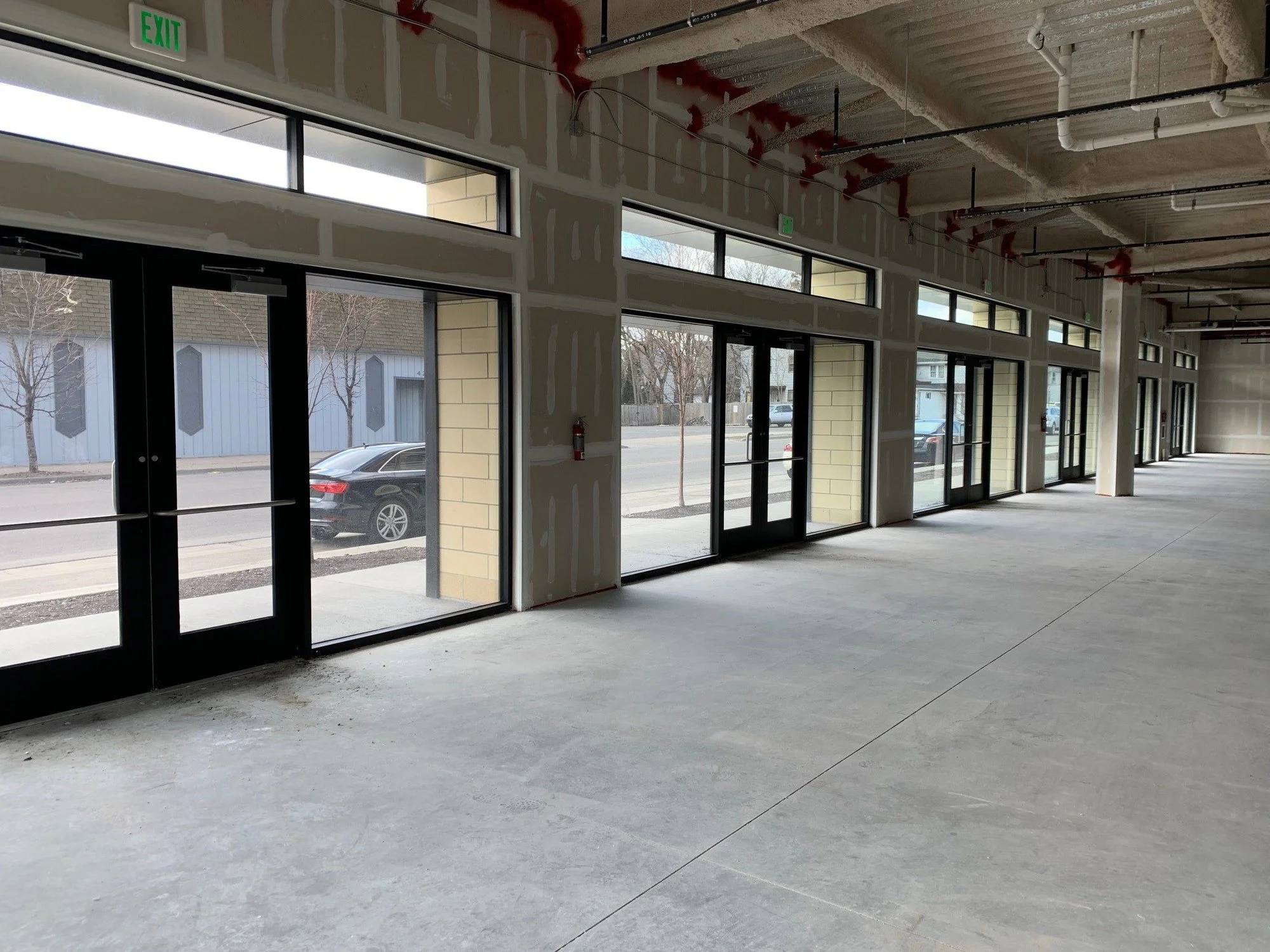 An empty modern office space with a glass-walled conference room, wood flooring, and an industrial-style ceiling with exposed ductwork.