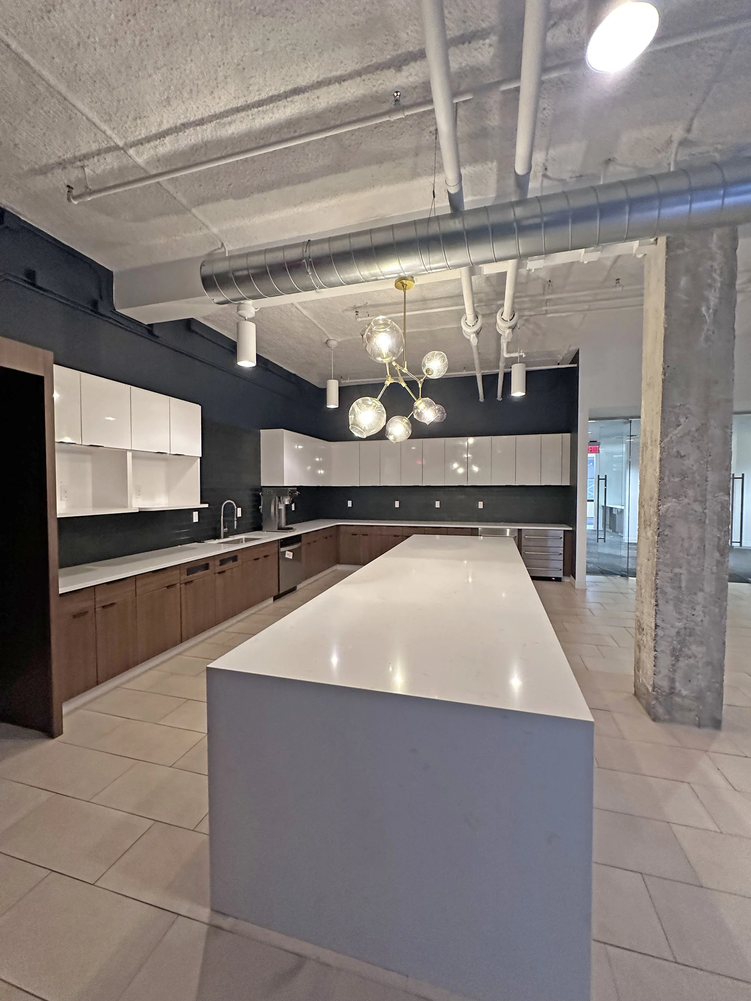Modern kitchen with a large white island, dark upper walls, white cabinets, stainless steel fixtures, and a decorative chandelier with glass globes.