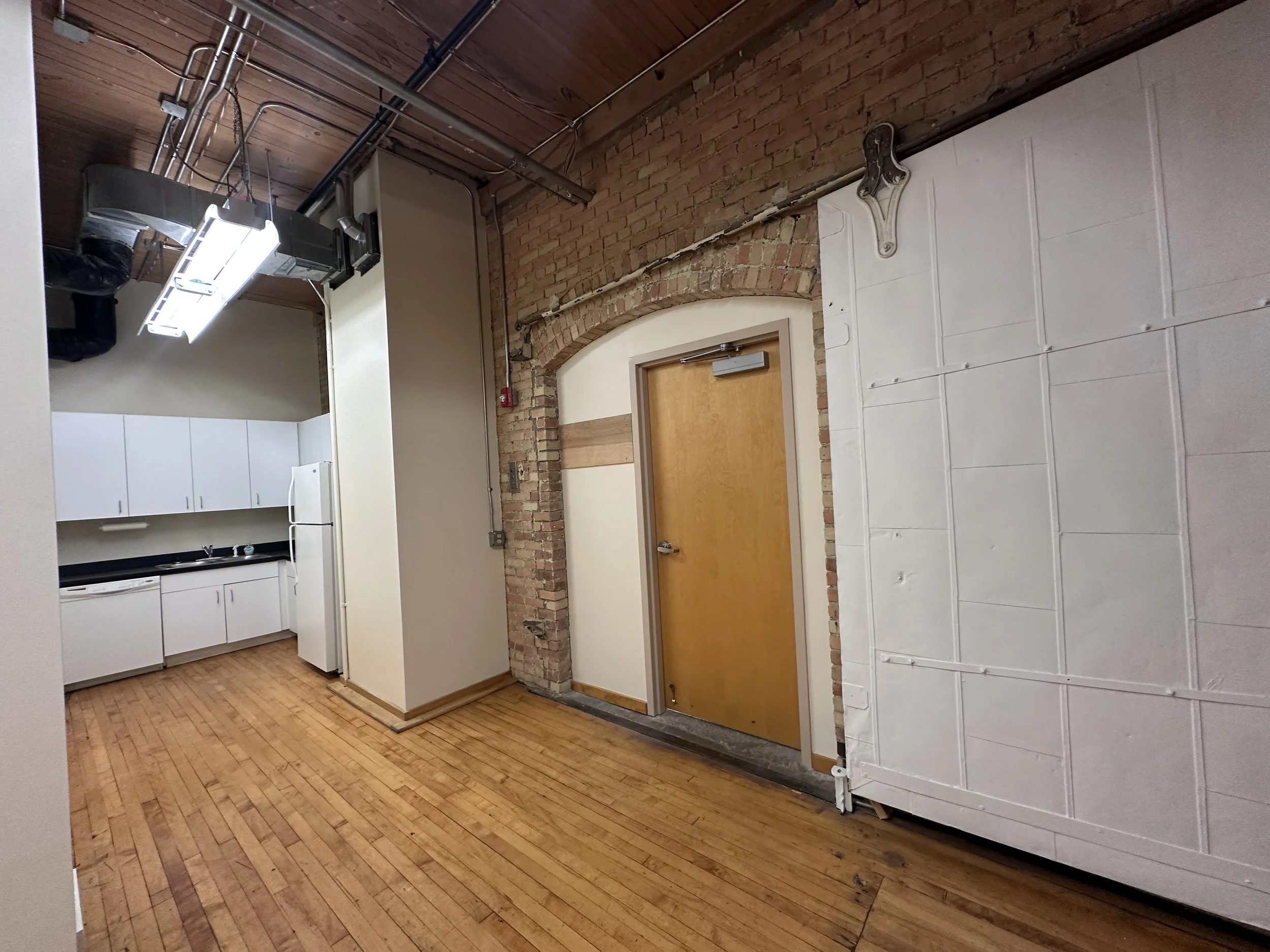 Interior of an industrial-style room with wooden flooring, exposed brick and a white paneled wall.