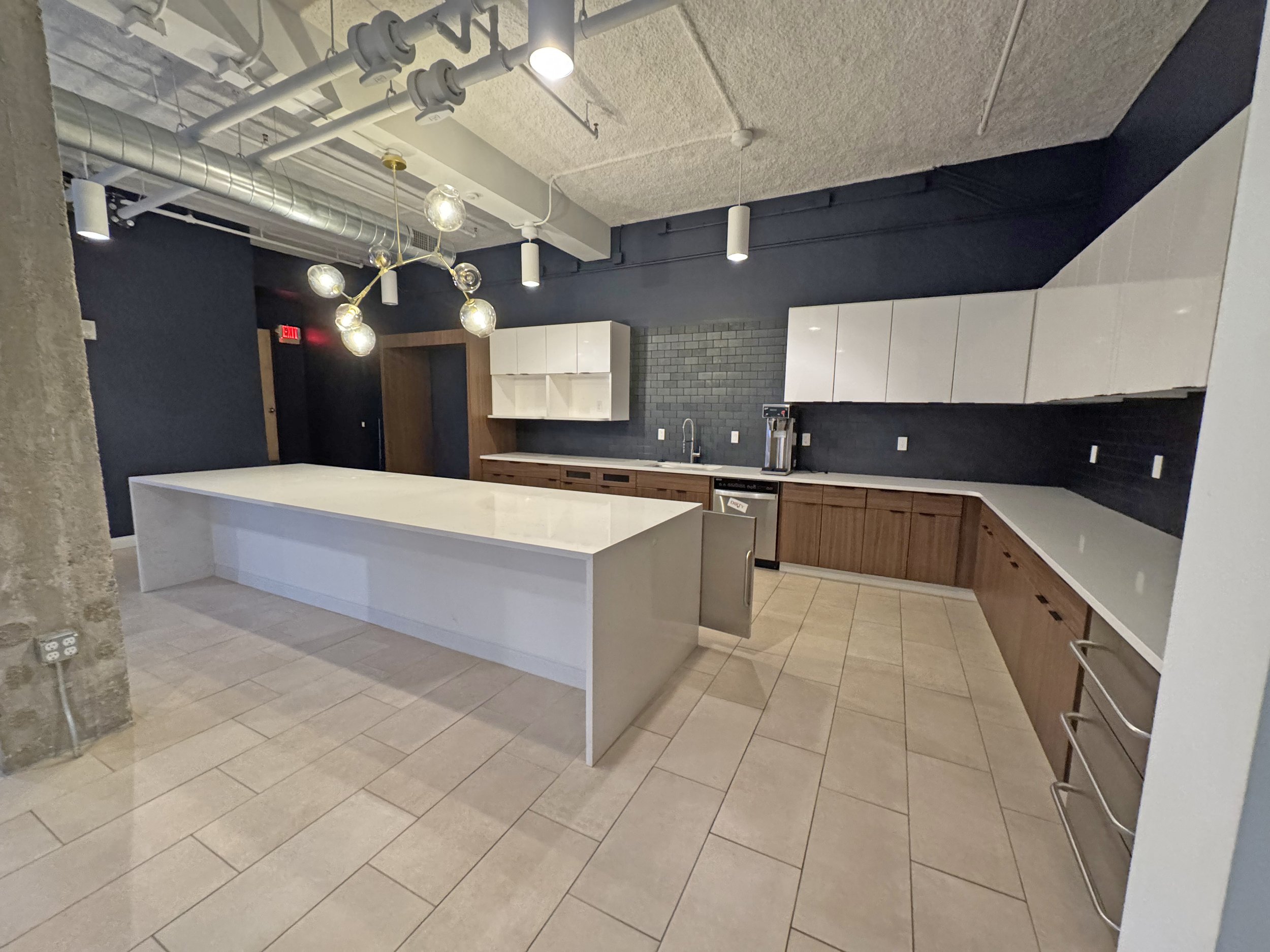 Modern kitchen with white island, dark blue and black walls, white and wood cabinets, pendant and ceiling lights, tiled floor.