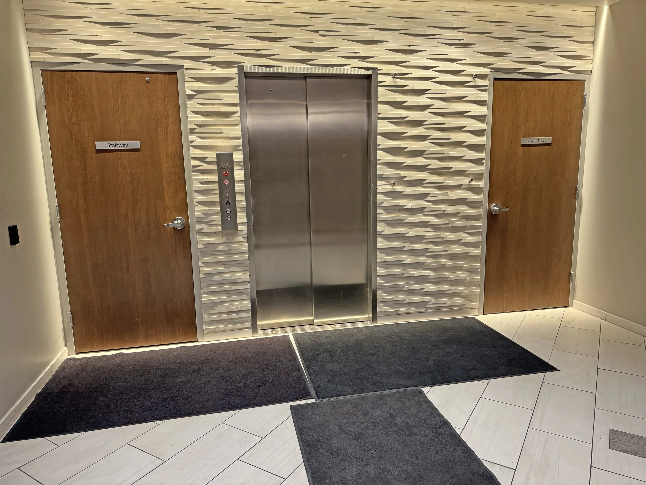 Elevator doors flanked by two wooden doors labeled "Stairway" and "Lower Level" in a modern building lobby.