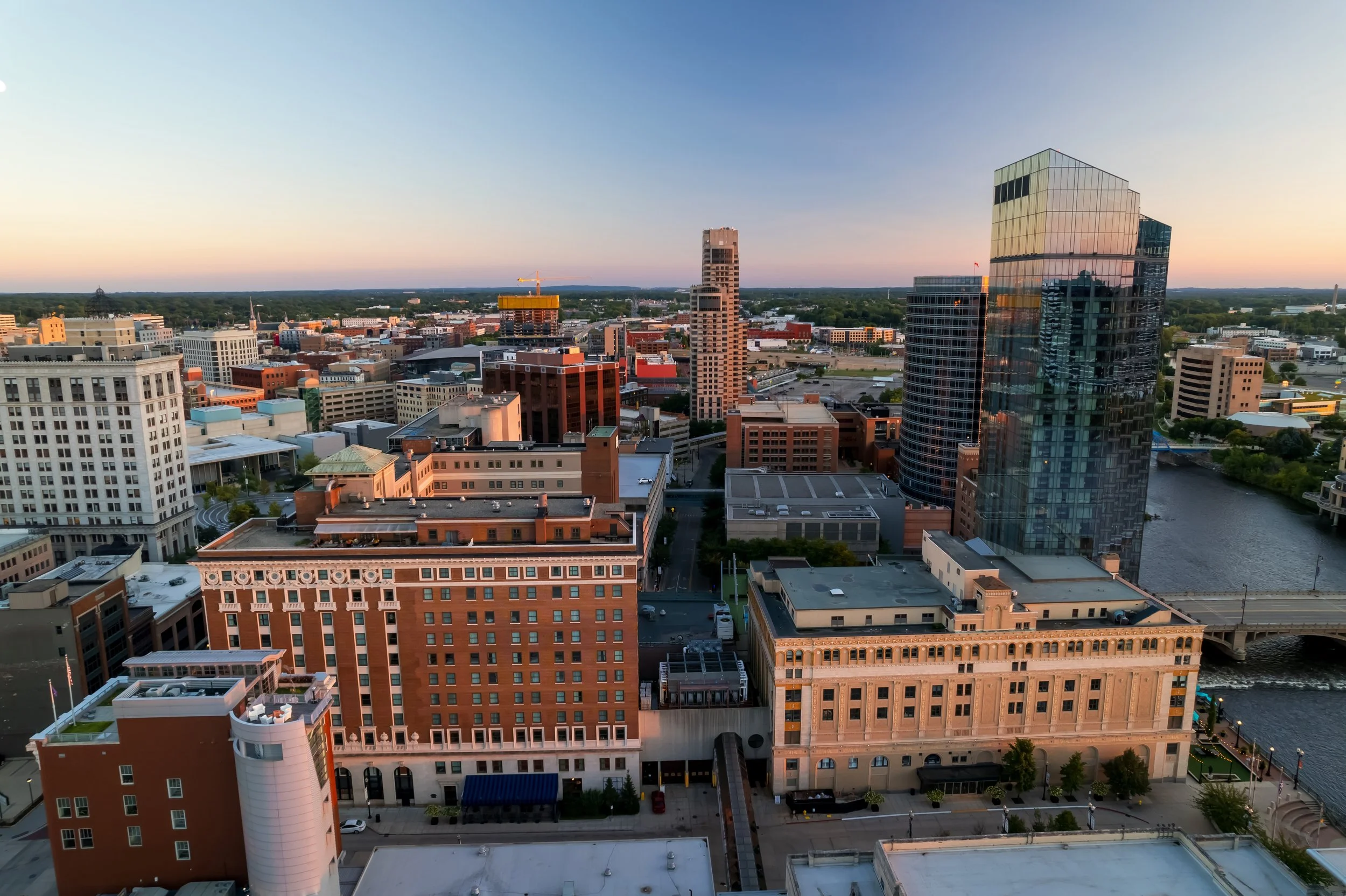Aerial view of a Grand Rapids skyline at sunset featuring various modern buildings, high-rises, and a river running through the city.