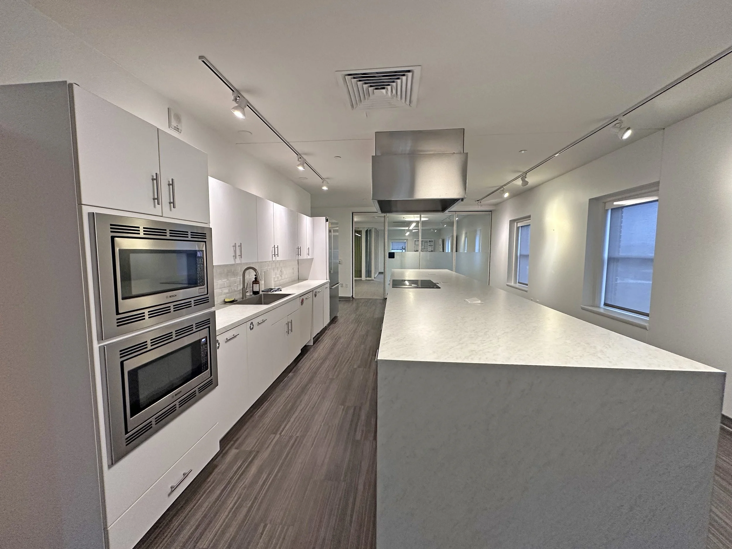 Modern kitchen with white cabinets, stainless steel appliances, marble countertop, and wood flooring.