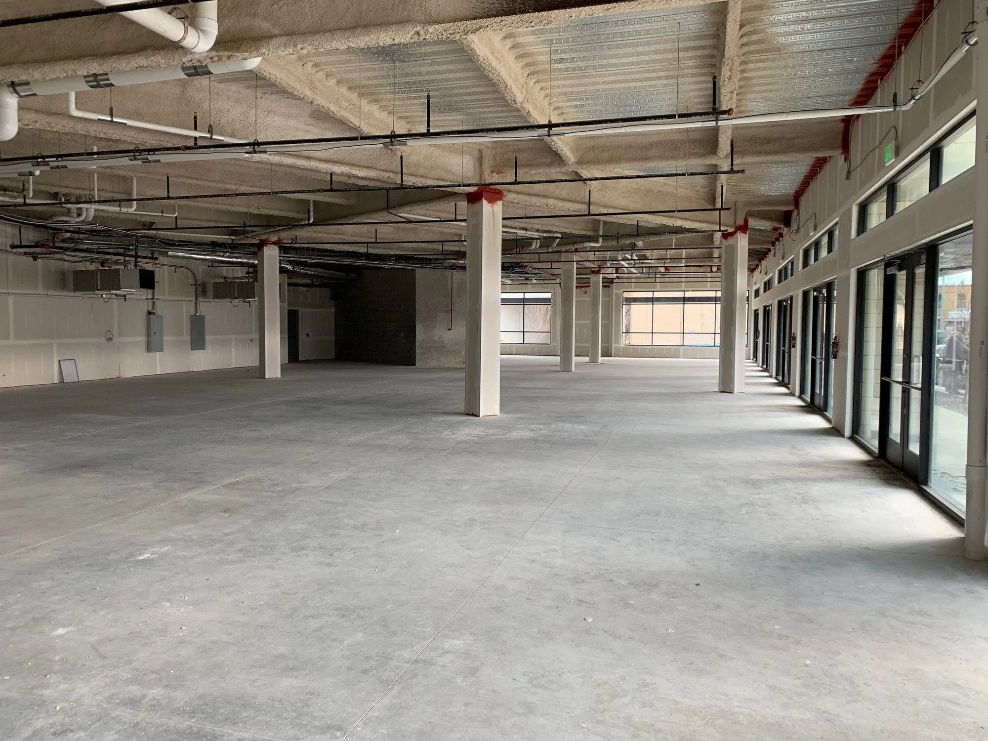 An empty room with three large windows, white walls, wooden flooring, and a black table leg in the corner.