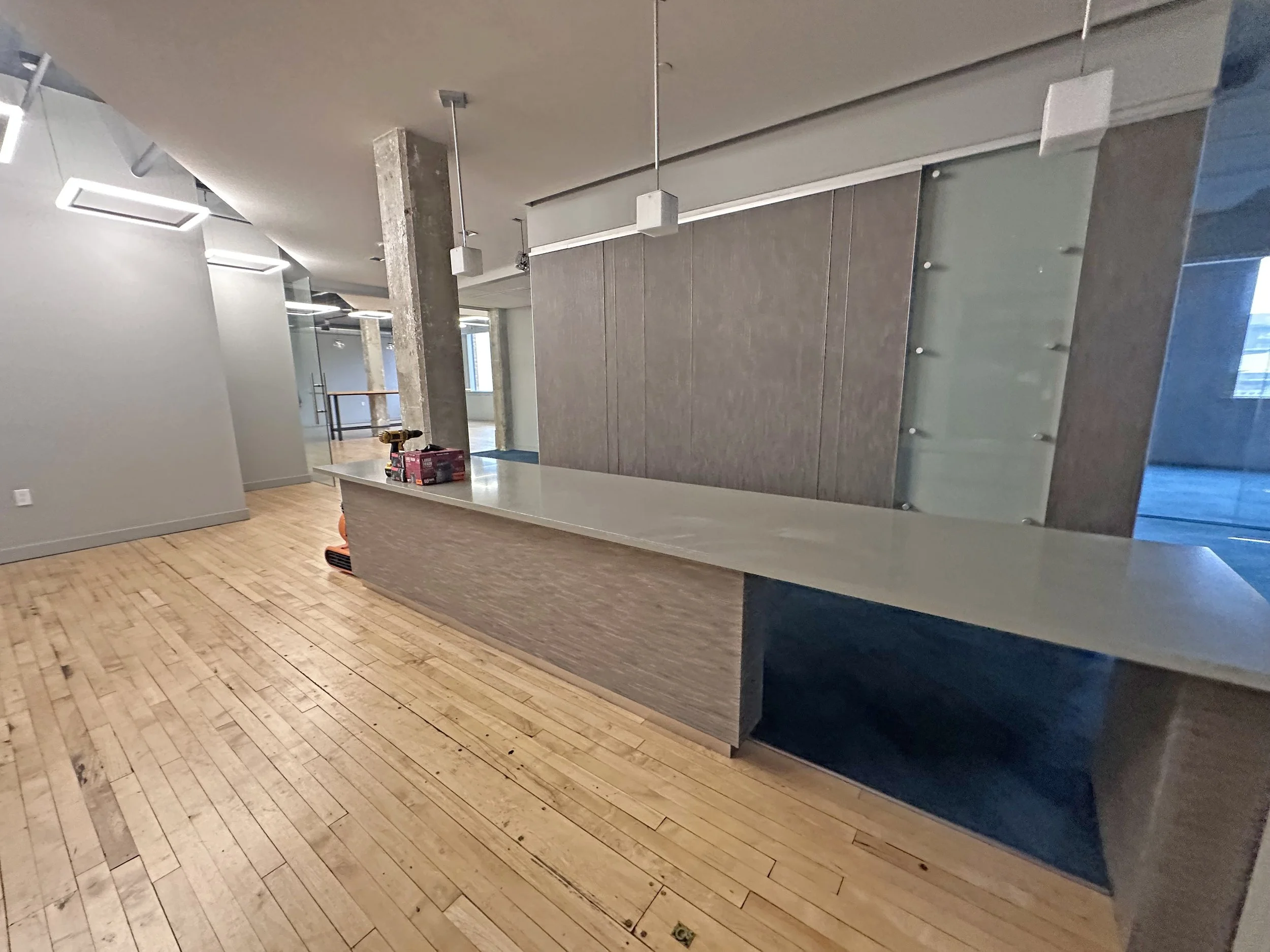 Interior of a modern building under construction, featuring a curved reception desk, wooden flooring, hanging pendant lights, and partially finished walls.