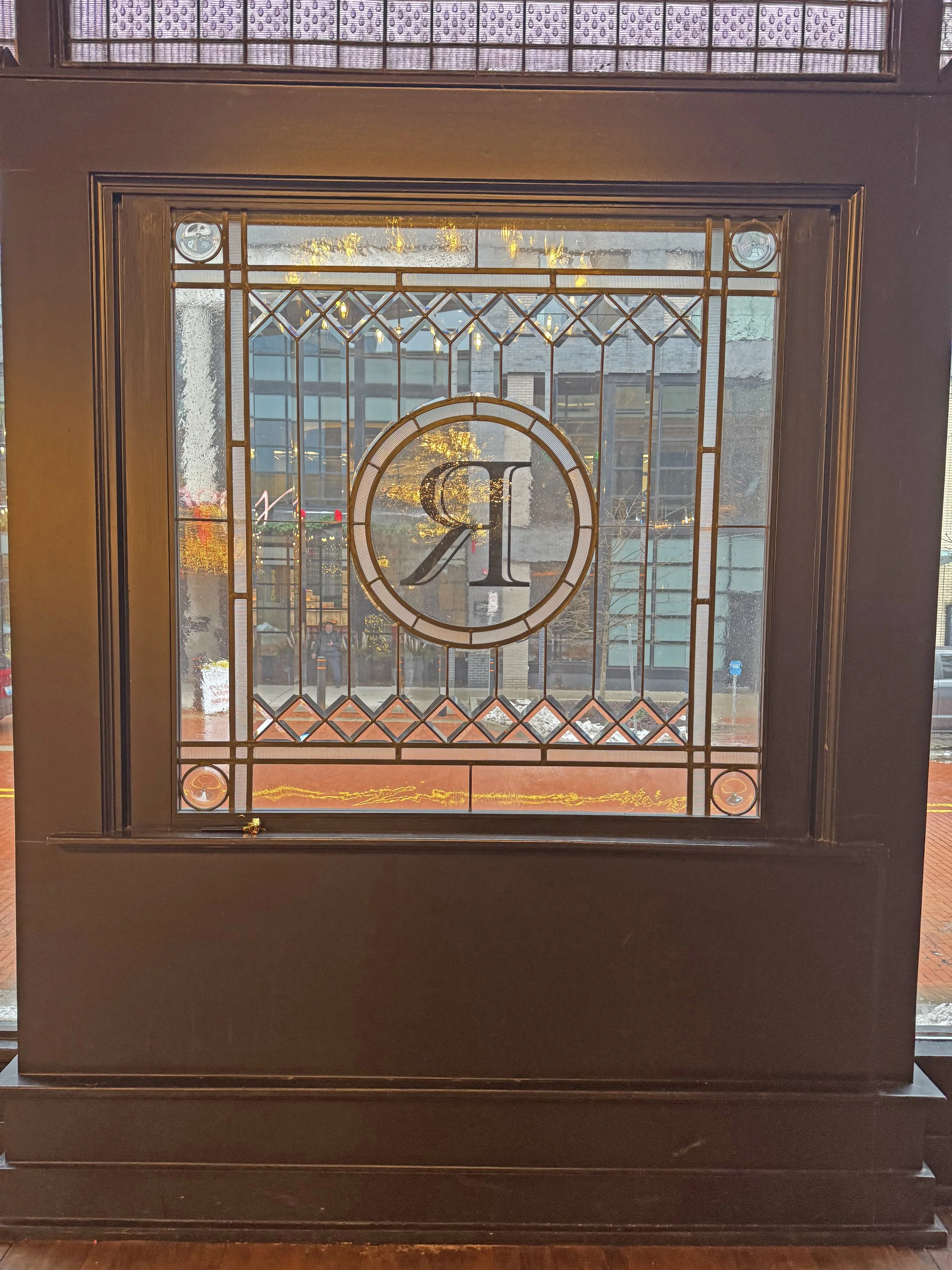 Decorative stained glass window with a monogrammed letter 'R' in the center, nestled within a dark wooden frame.