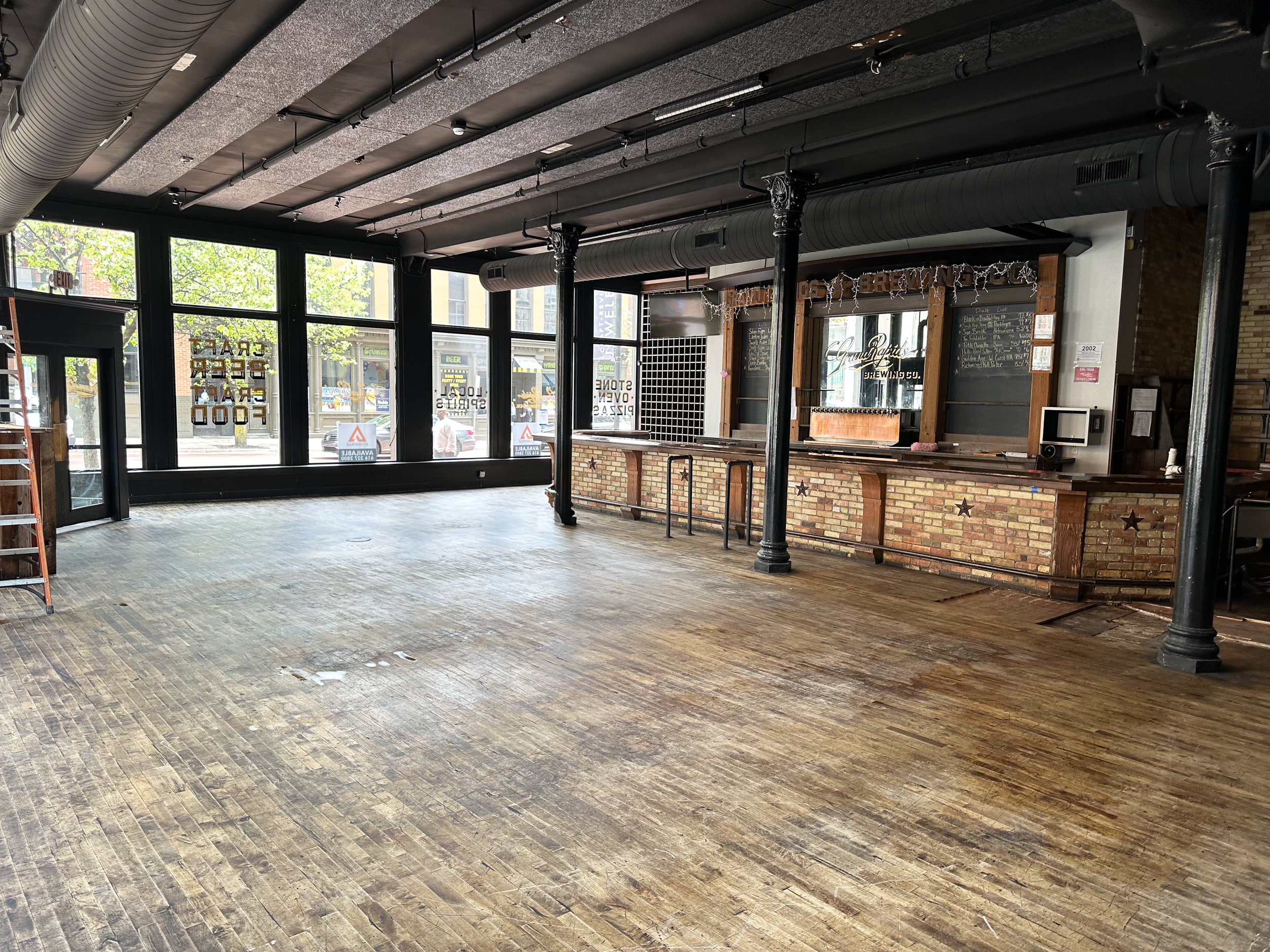 An empty room with three large windows, white walls, wooden flooring, and a black table leg in the corner.