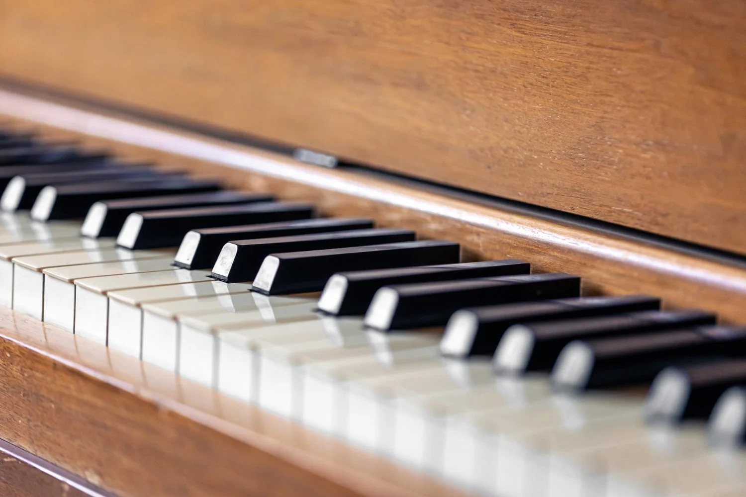Close-up of a piano keyboard with black and white keys, showing part of the wooden piano body.