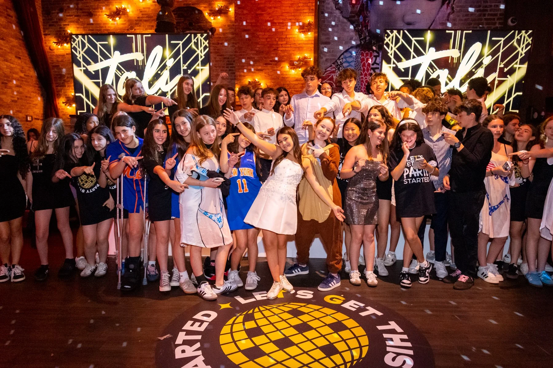 A group of teenagers gathered on a stage under warm lighting, with two large digital screens displaying the word 'Tackle' behind them, and a circular logo on the floor that mentions 'United.