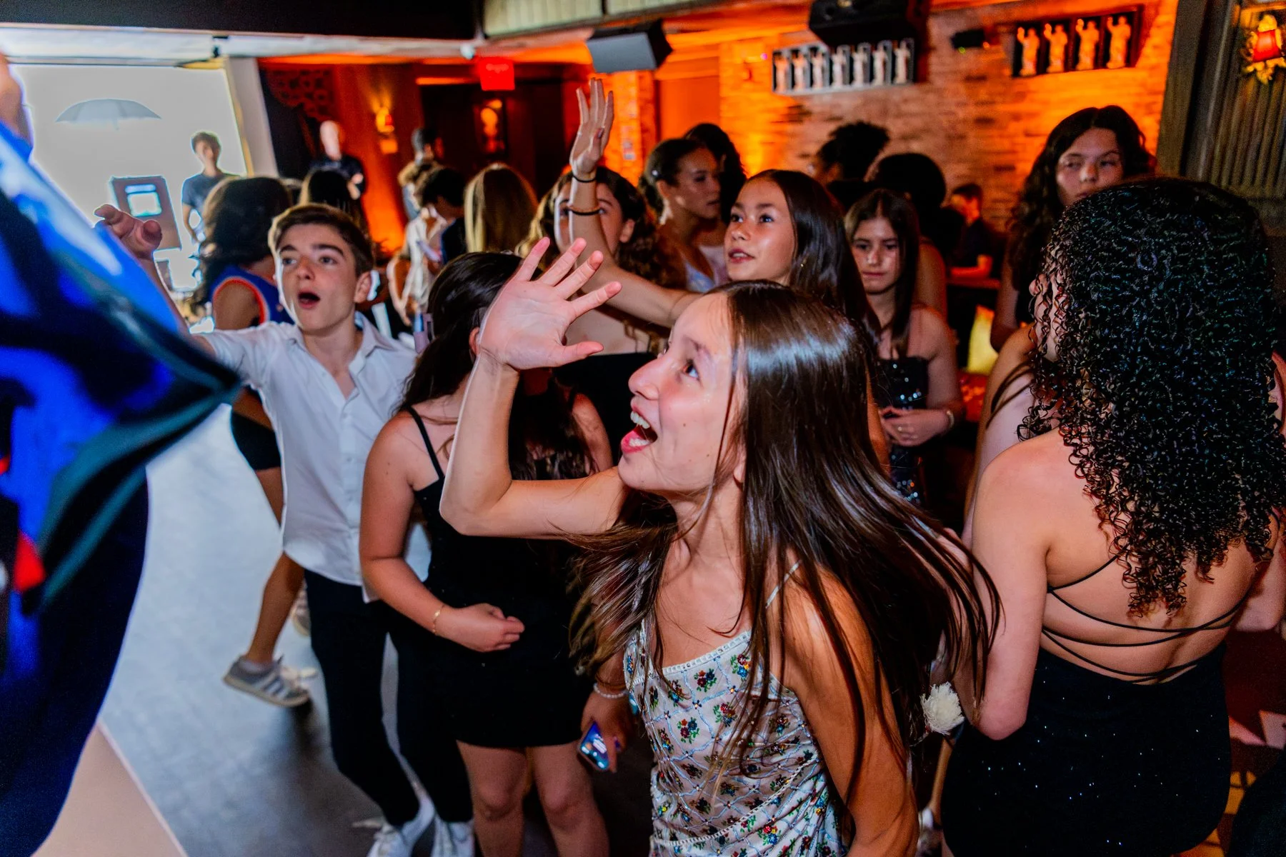 A group of people dancing and socializing in a dimly lit bar or club with wooden walls and wall-mounted decorations, engaged in lively conversation and dance.