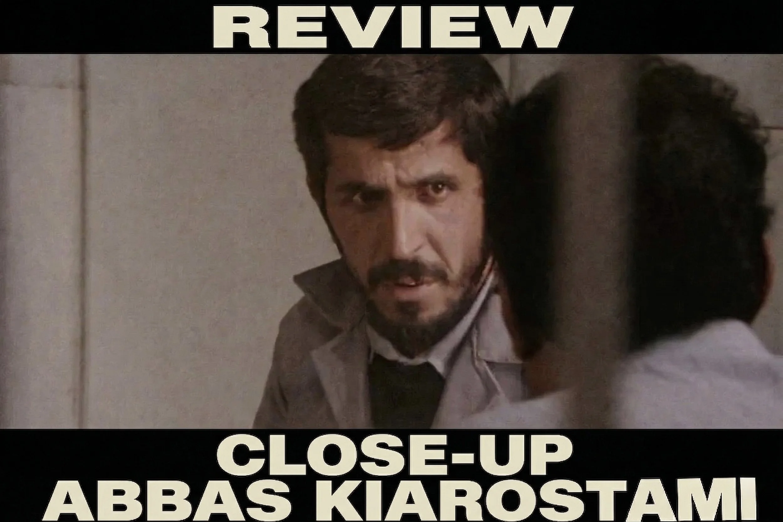 Un hombre con barba y cabello oscuro tiene una expresión de enojo o concentración, y está en un espacio interior con paredes de color claro. La imagen parece ser parte de una reseña o análisis, con texto en la parte superior e inferior que dice: 'REVIEW' y 'CLOSE-UP ABBAŠ KIAROSTAM'.