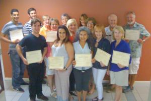 A group of adults, some holding certificates, posing together indoors against a reddish wall.
