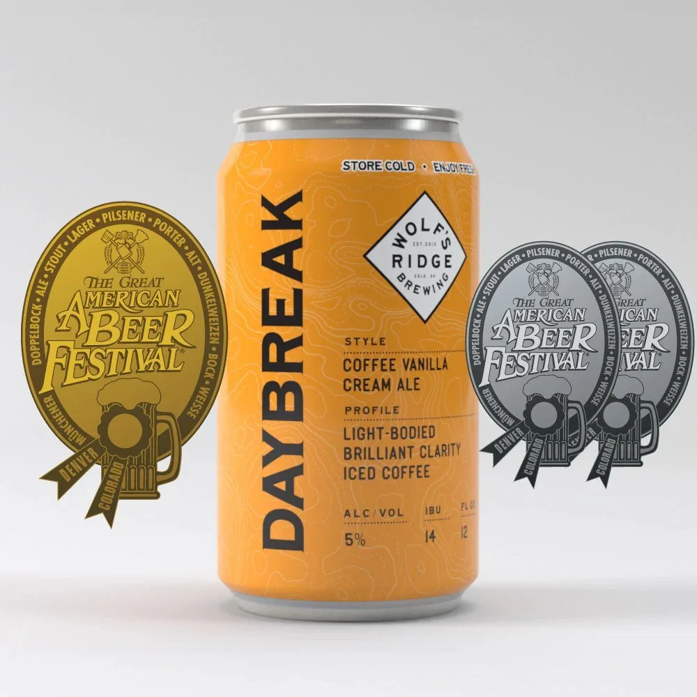 An orange can of Wolf's Ridge Daily Break Coffee Vanilla Cream Ale with a silver top, positioned between two festival medals for the American Beer Festival, one gold and one silver, featuring beer mugs and ribbons.
