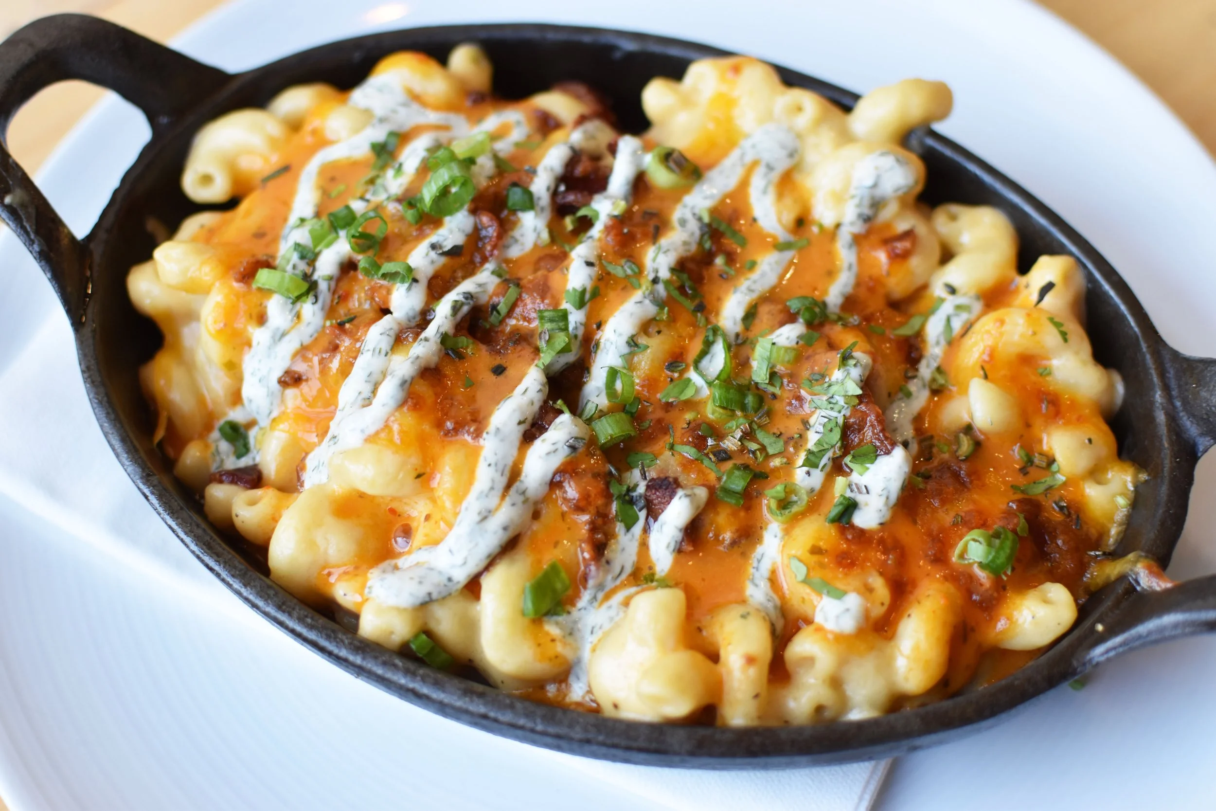 Baked macaroni and cheese in a cast iron skillet garnished with chopped green onions and drizzled with white sauce.