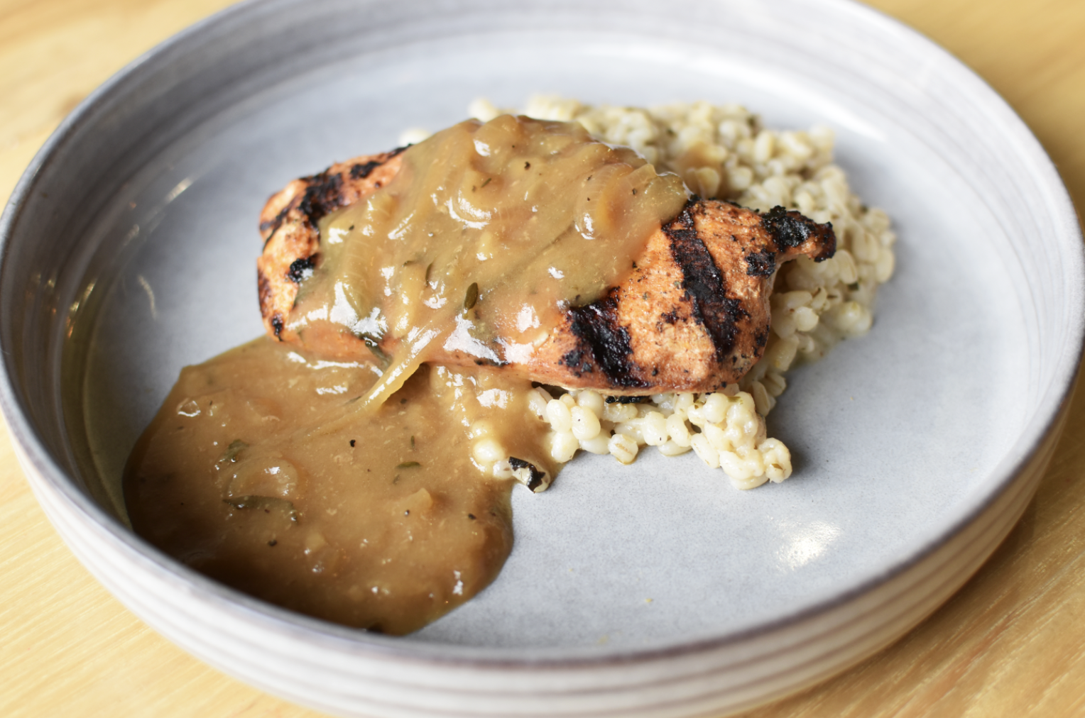 Grilled chicken breast topped with gravy, served with a side of cooked barley or rice.