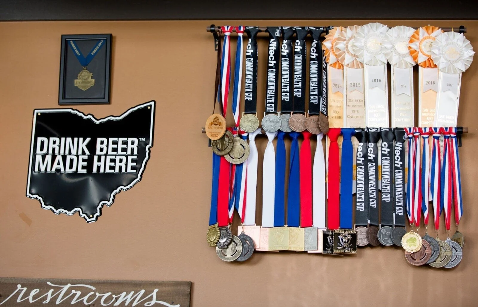 Medals and ribbons hanging on a wall next to a sign that says "Drink Beer Made Here" with a silhouette of Ohio filled in black.