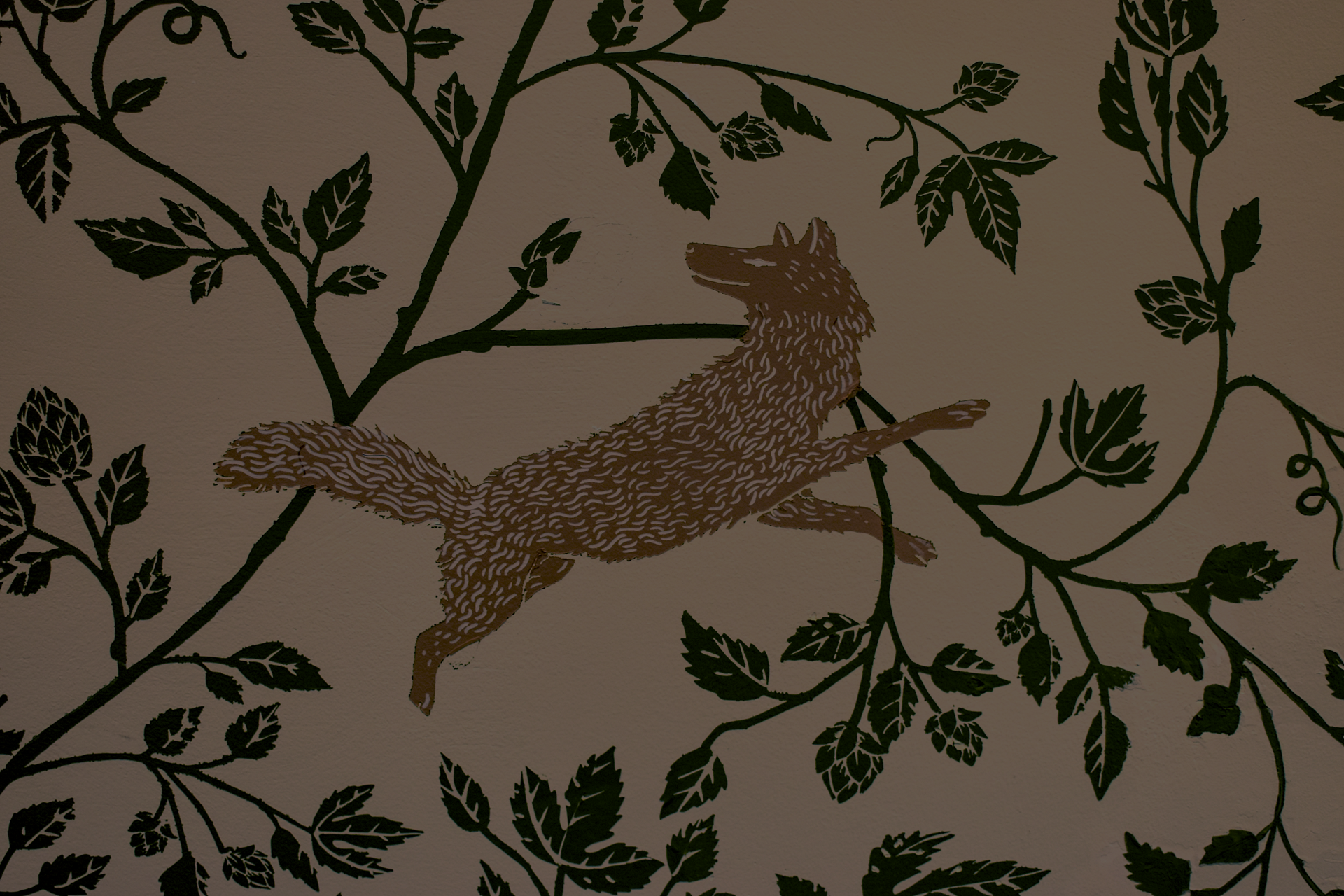 Indoor wedding ceremony with guests seated on both sides, three women standing at the altar, large windows letting in natural light, wooden flooring, and modern chandeliers hanging from the ceiling.