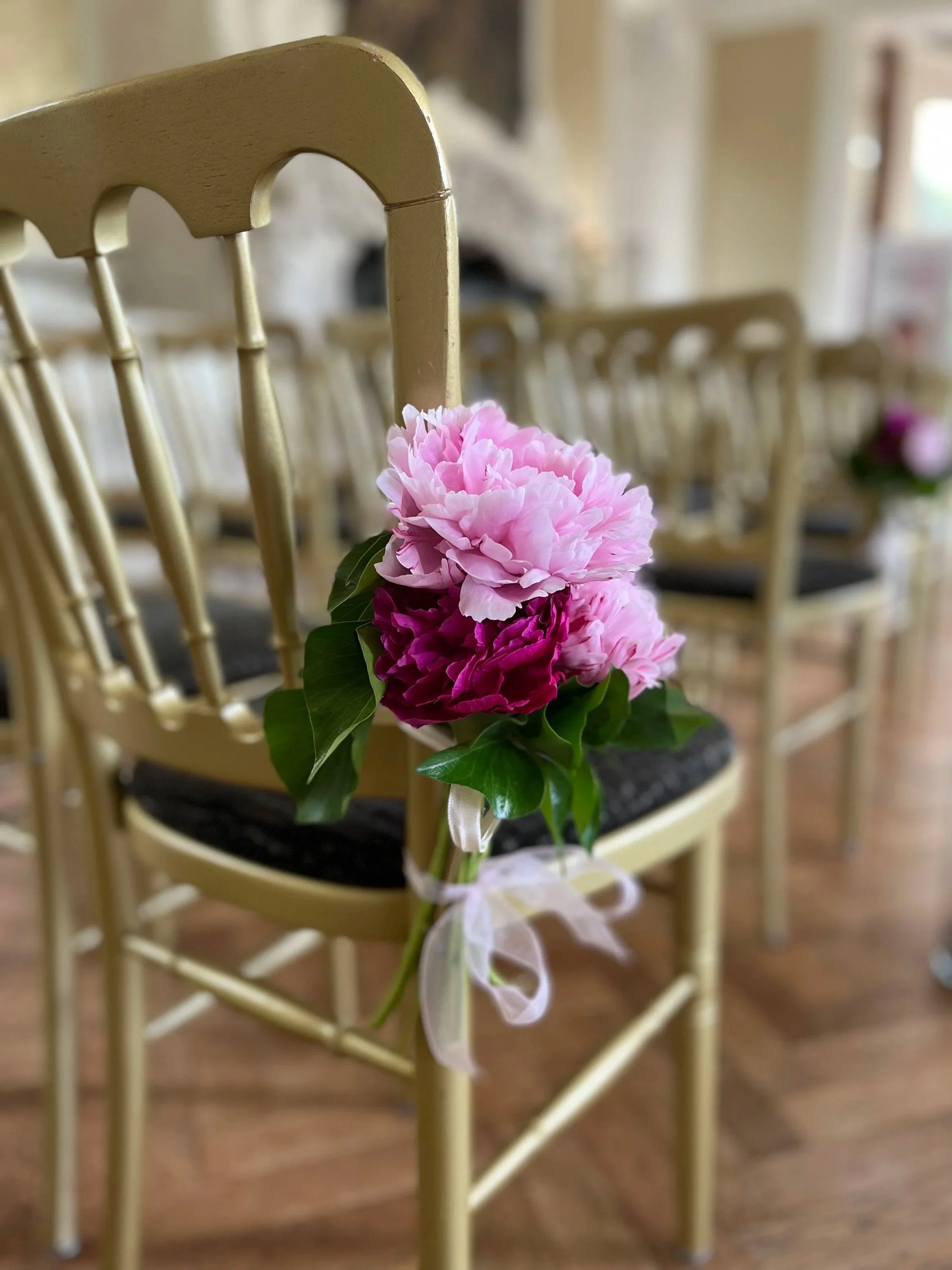 A bouquet of pink and purple carnations tied with a white ribbon and attached to a beige dining chair at a formal event.