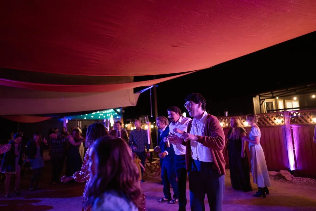 People dancing and socializing at an outdoor party or celebration under colorful string lights at night.