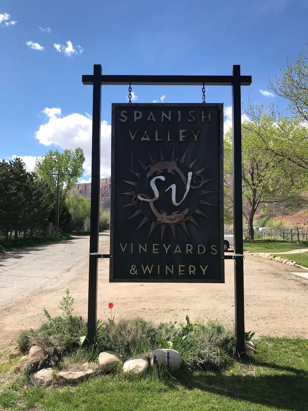 Sign for Spanish Valley Vineyards & Winery with a desert landscape, trees, and a blue sky in the background.