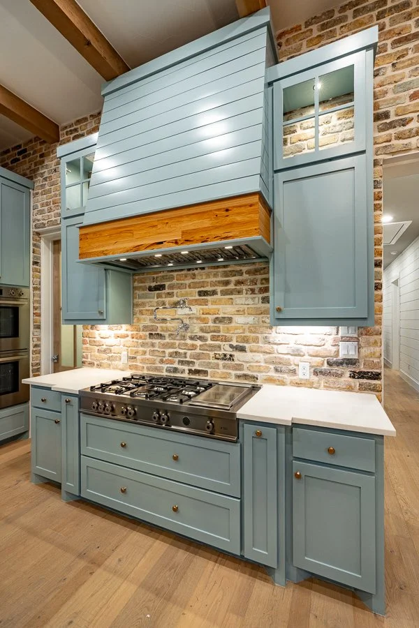Kitchen with blue cabinets, brick wall backsplash, a range with oven, and a large blue range hood.