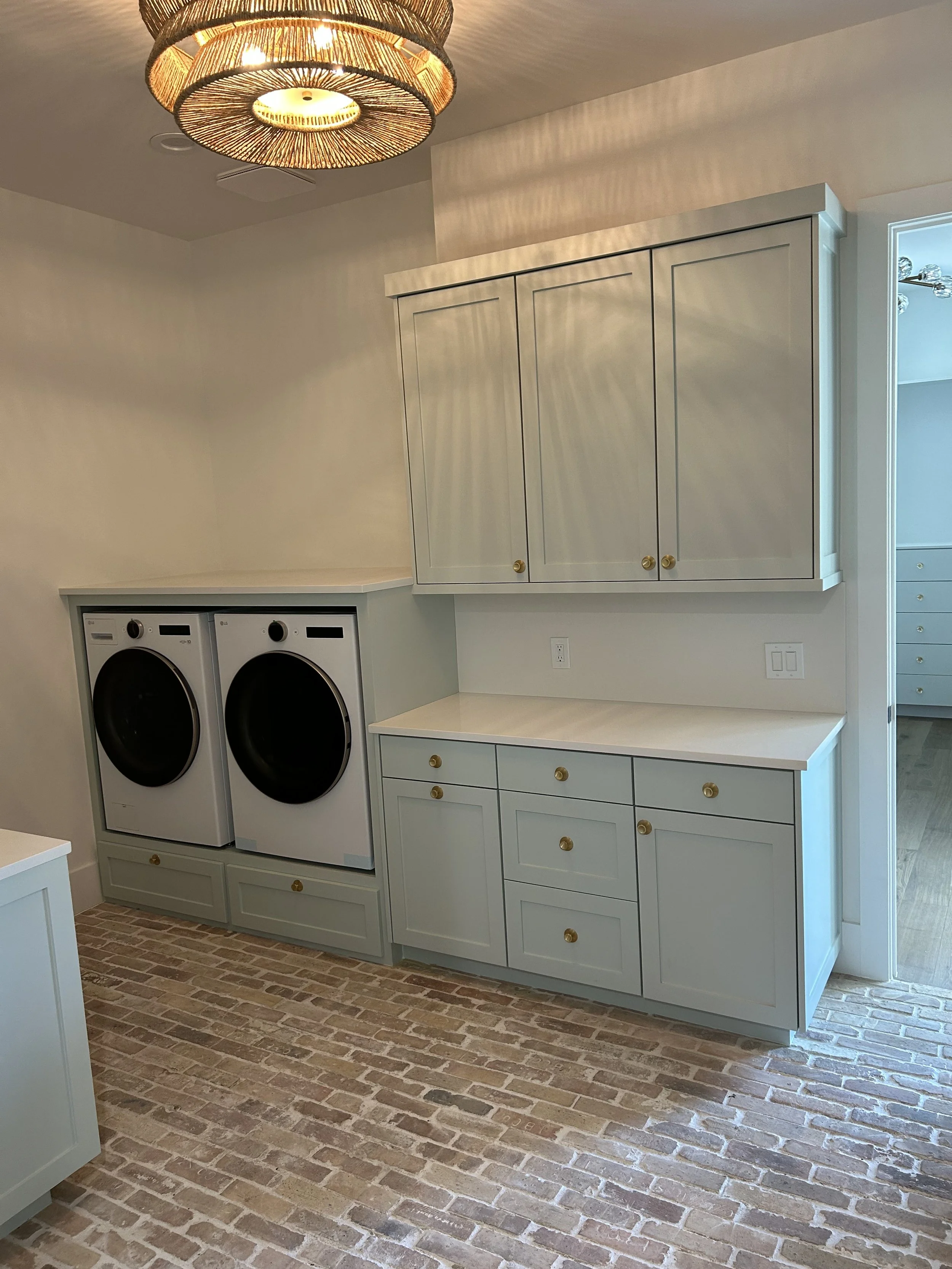 Laundry room with a washer and dryer, white cabinets with gold knobs, and a brick-style floor.