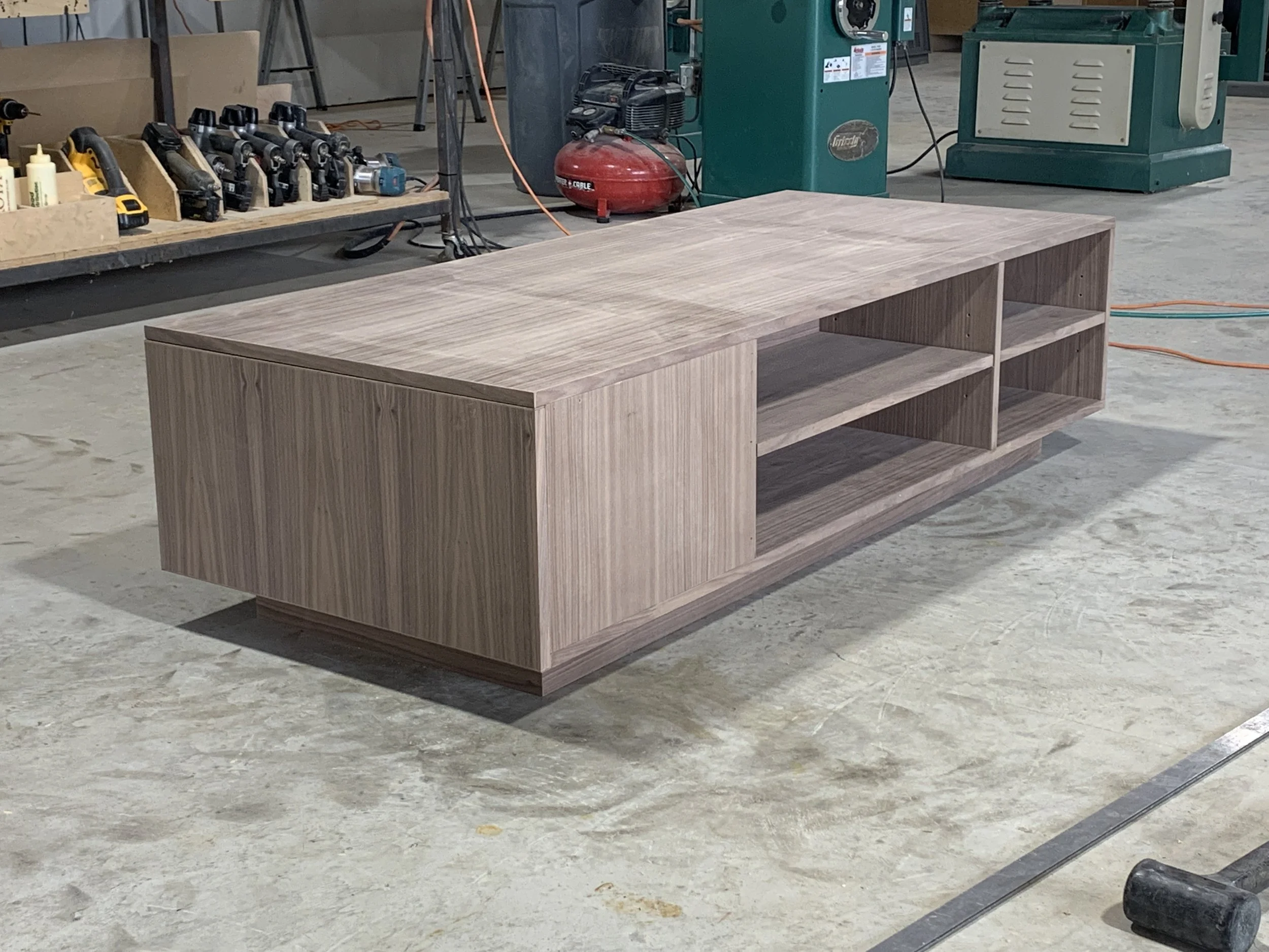 unfinished wooden TV stand with open shelves in a woodworking workshop.