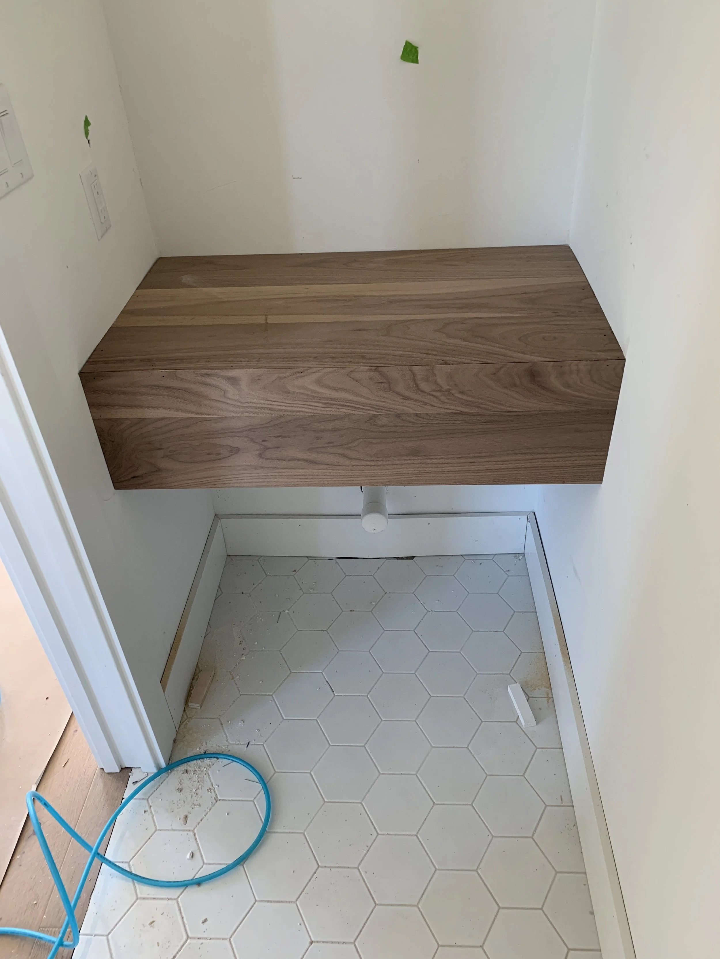 An empty bathroom corner with hexagon floor tiles, a wooden vanity, and a pipe protruding from the wall.