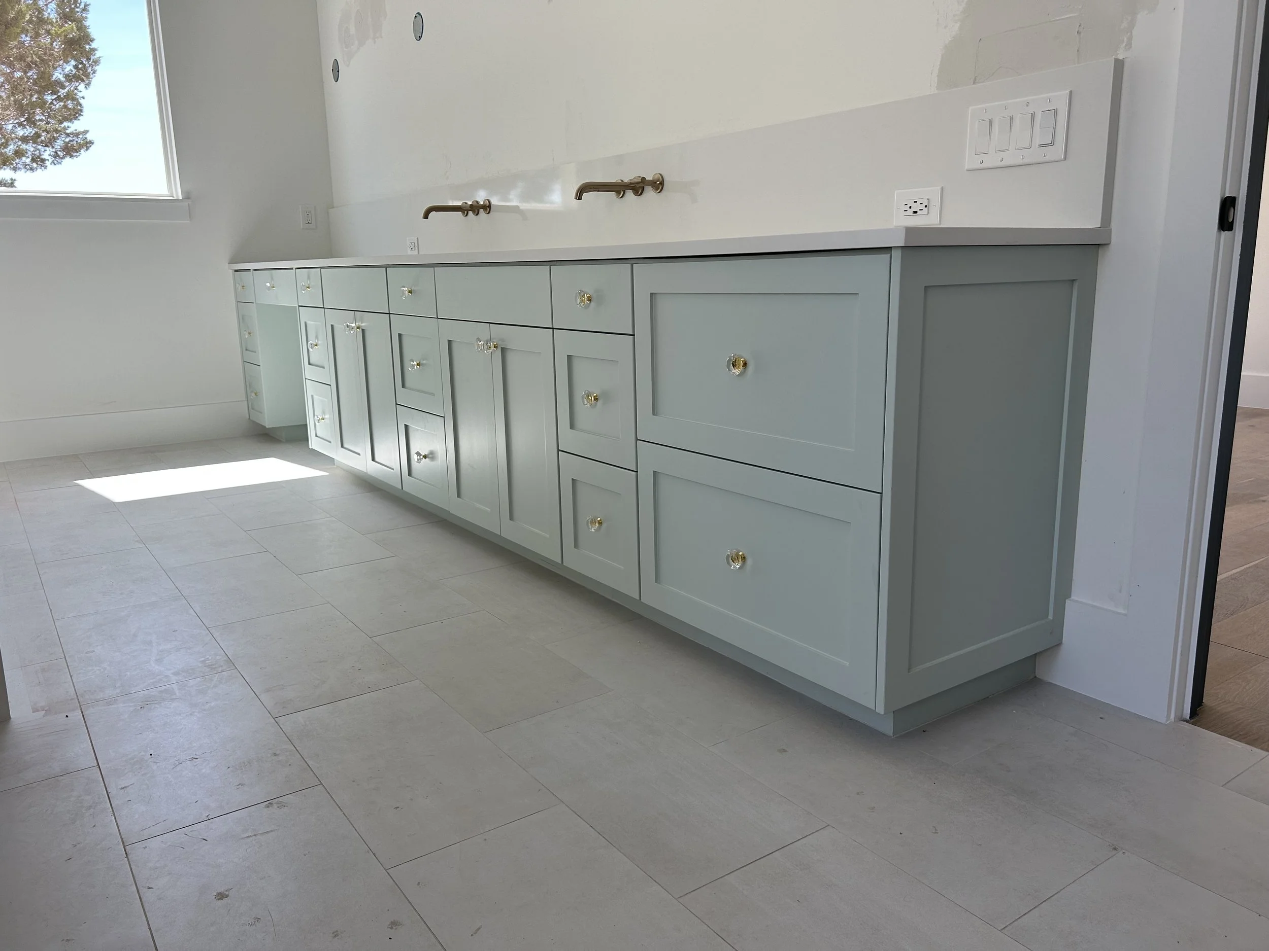 Light blue kitchen cabinets with gold knobs and a white countertop, located in a room with white walls and tile flooring.