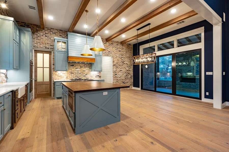 Modern kitchen with blue cabinetry, wooden island, exposed brick wall, and large sliding glass doors leading outside.