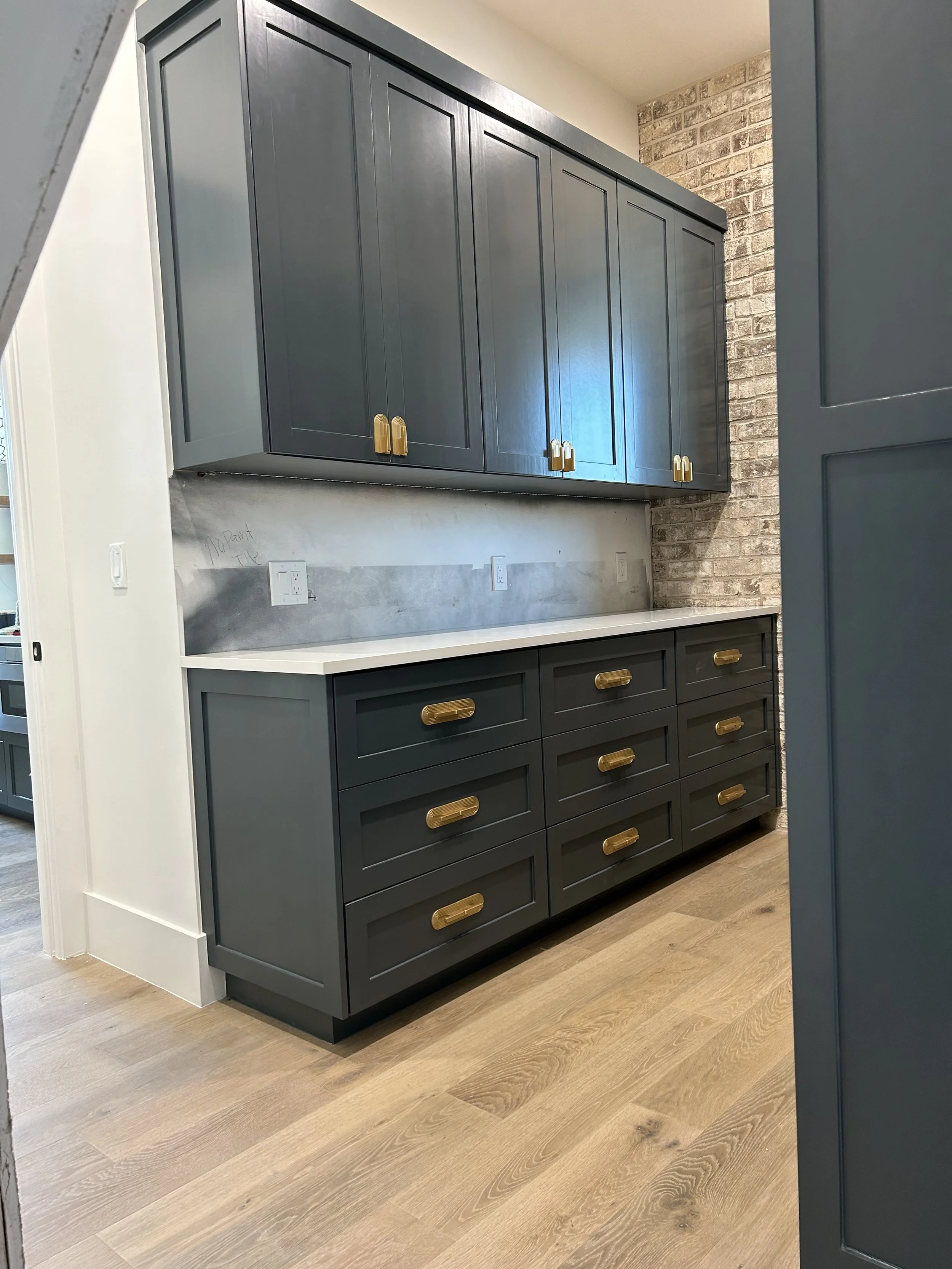 Kitchen with dark blue cabinets, brass handles, wood flooring, and a brick accent wall.