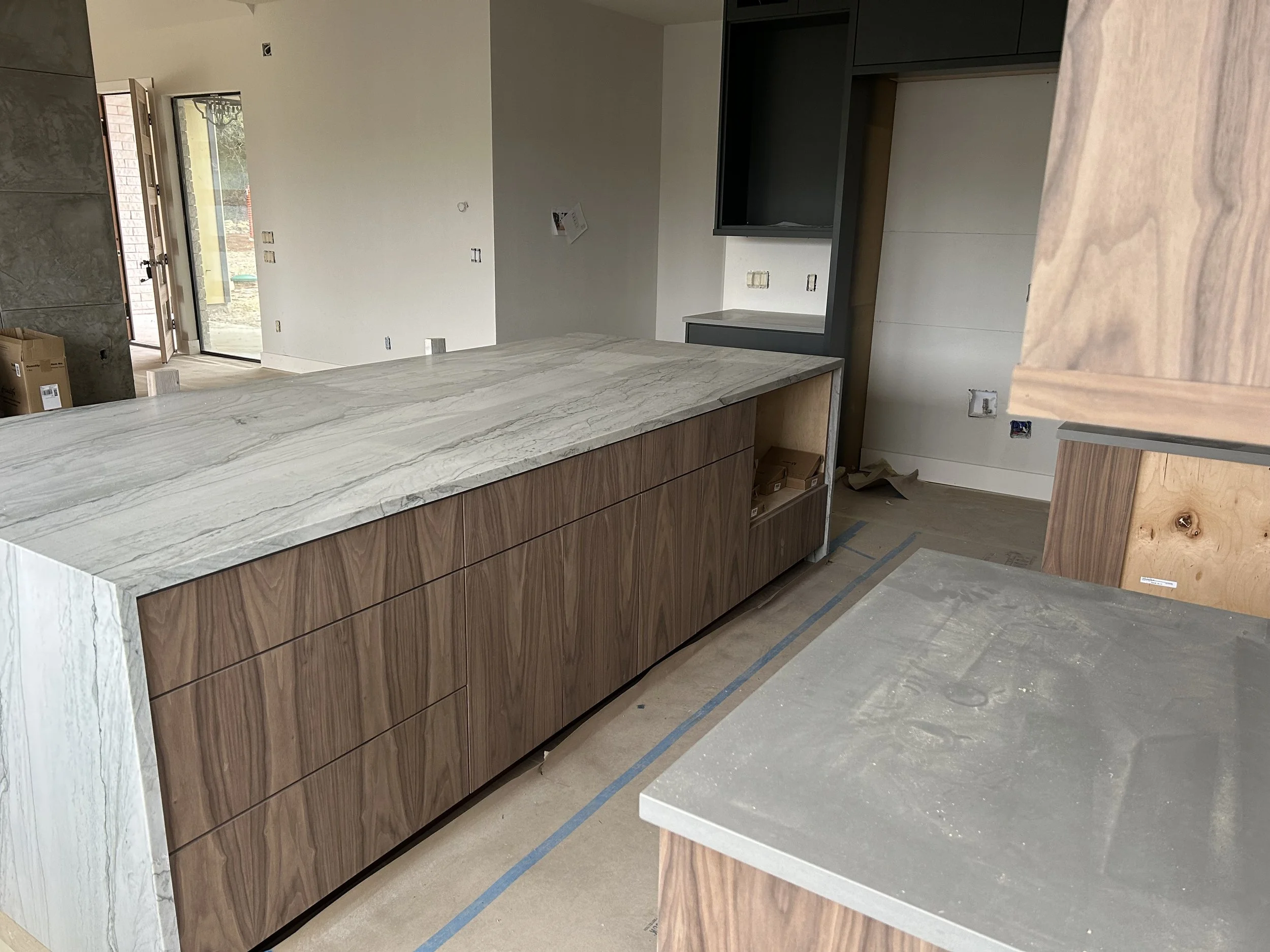 A modern kitchen under construction with a marble countertop, wooden cabinets, and unfinished walls and floors.