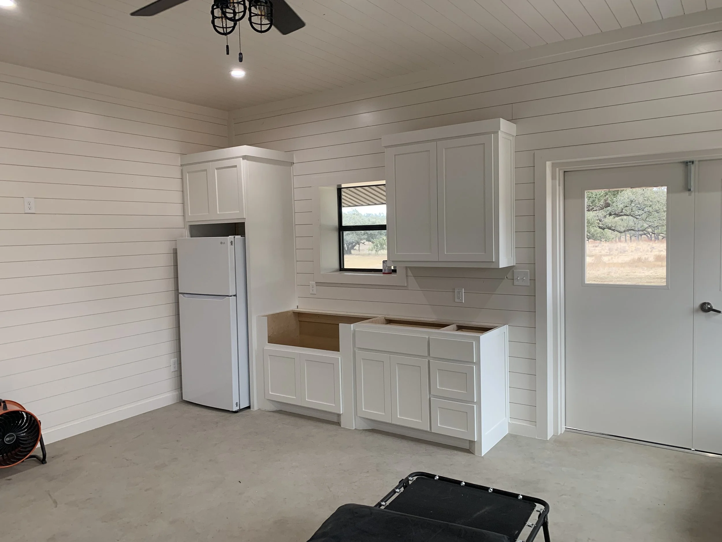 Interior of a partly finished kitchen with white cabinets, a new refrigerator, and an unfinished base cabinet.