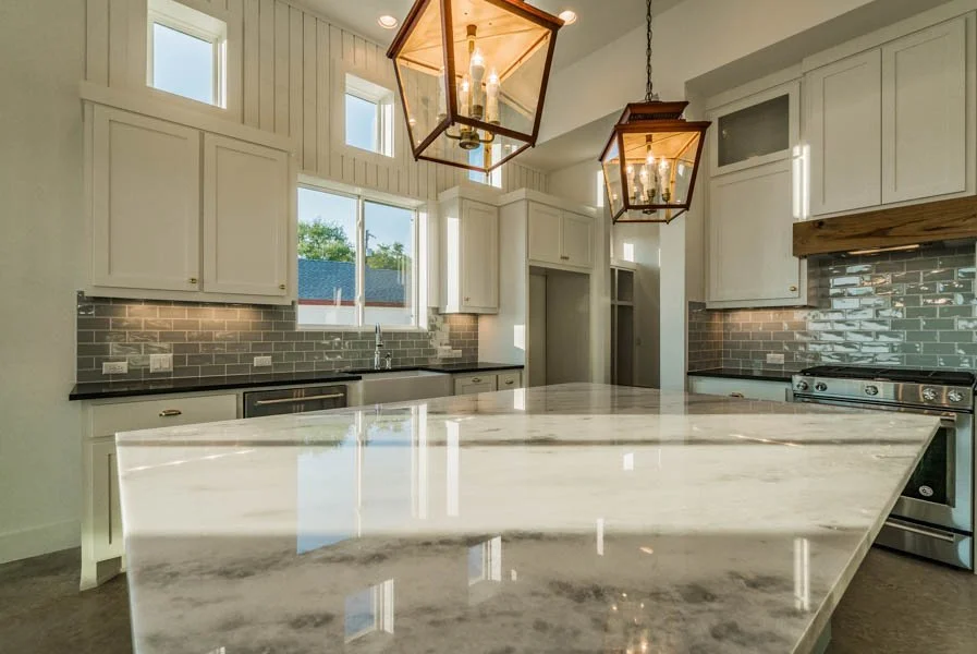 Modern kitchen with white cabinets, a large marble island, gray subway tile backsplash, stainless steel appliances, and two geometric pendant lights.