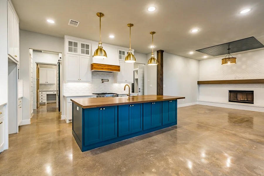 Modern kitchen with white cabinetry, a blue island, gold pendant lights, a gas stove, and a wooden countertop.