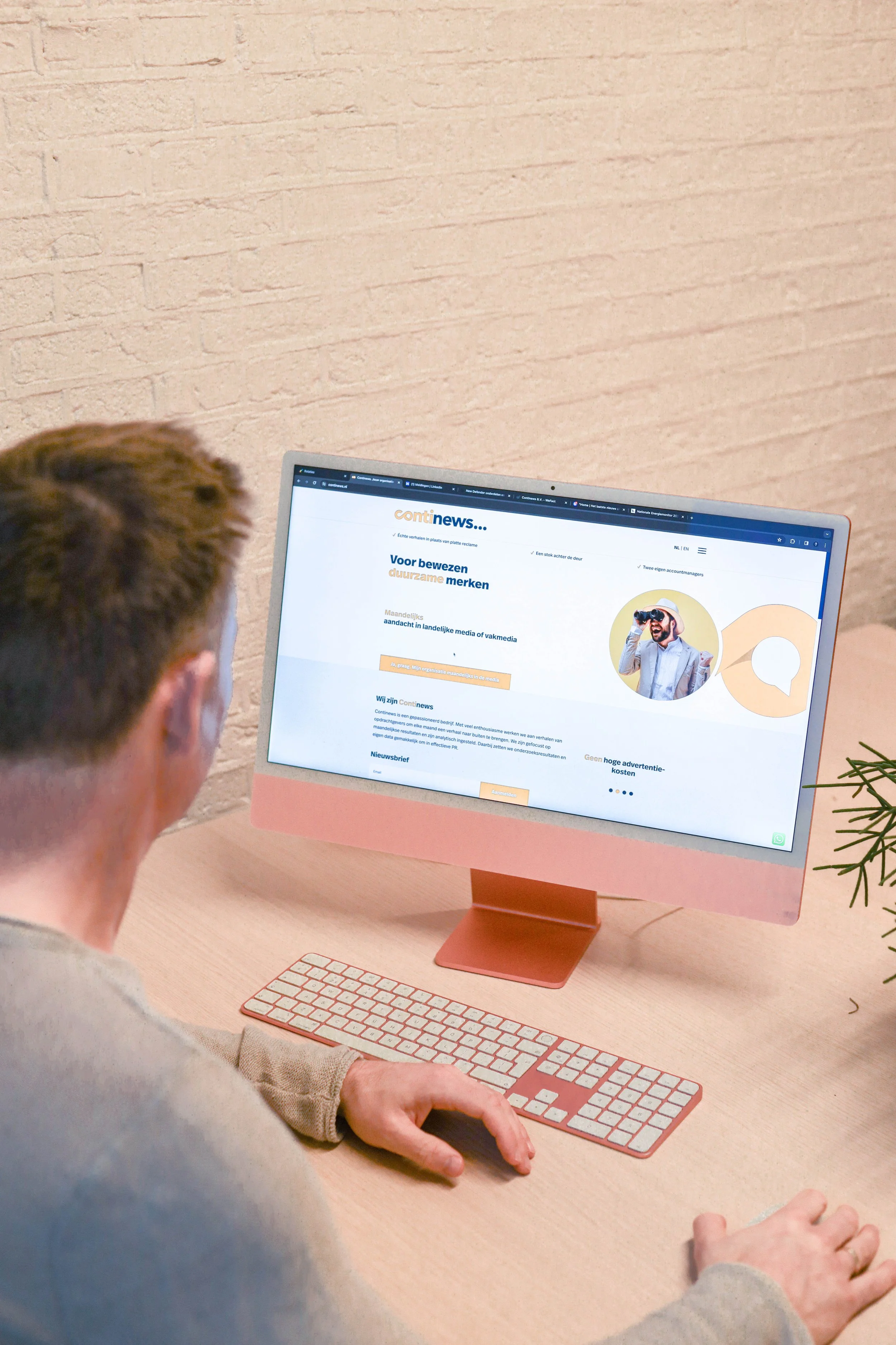 Person som bruker en dataskjerm med nettside for nyhetsbrev av kontinews, på et skrivebord med en liten plante til høyre.