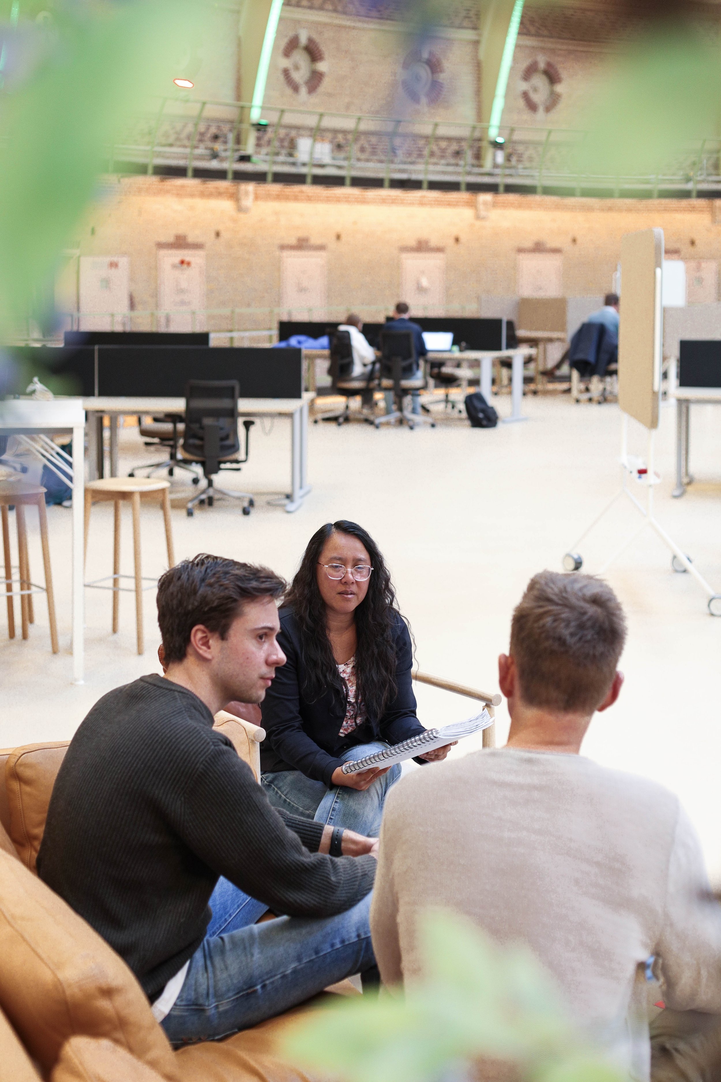 Tre personer som diskuterer i et kontormiljø med flere arbeidsstasjoner og kontorstoler i bakgrunnen.