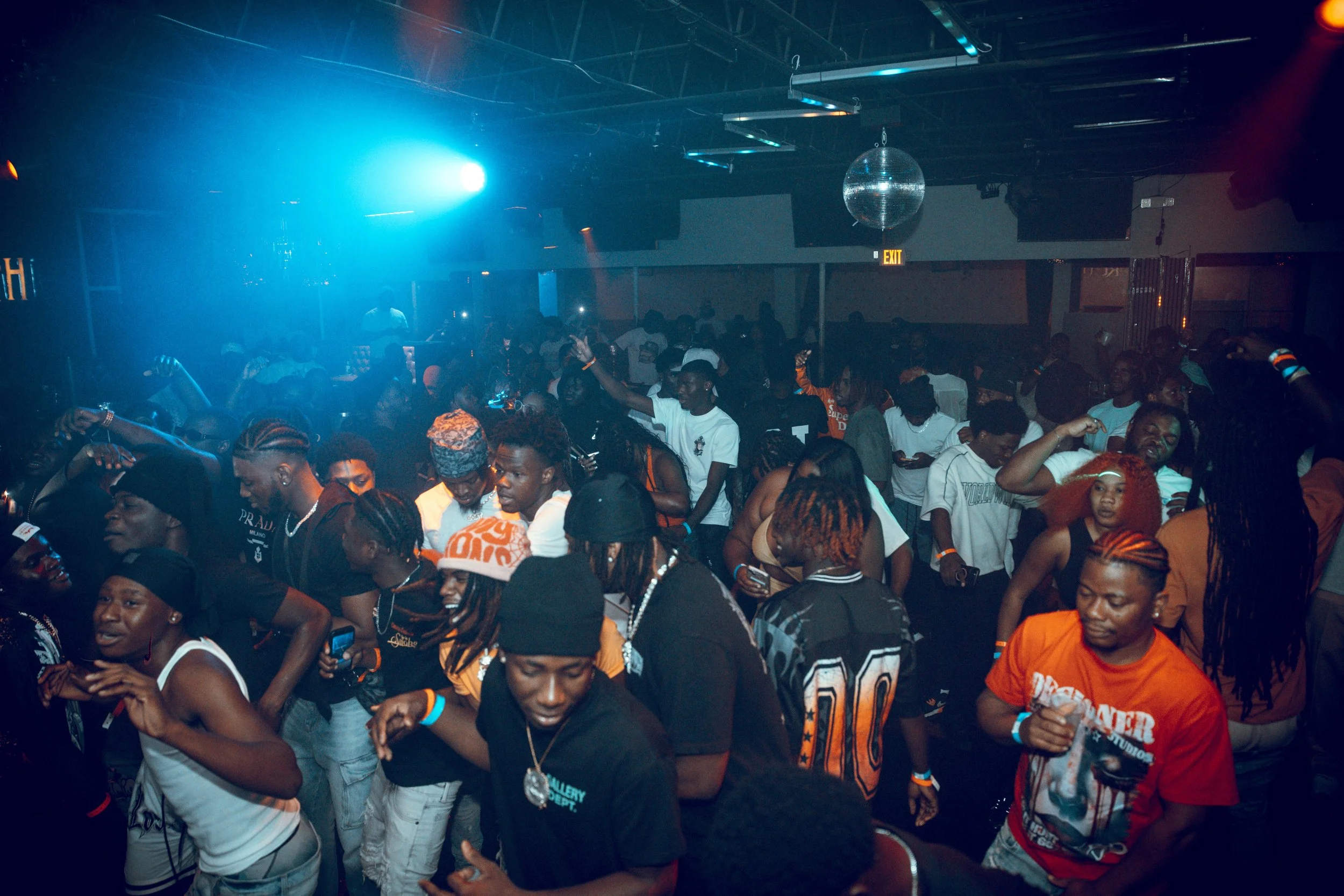 Crowd of people dancing in a nightclub with colorful lighting and a disco ball overhead.