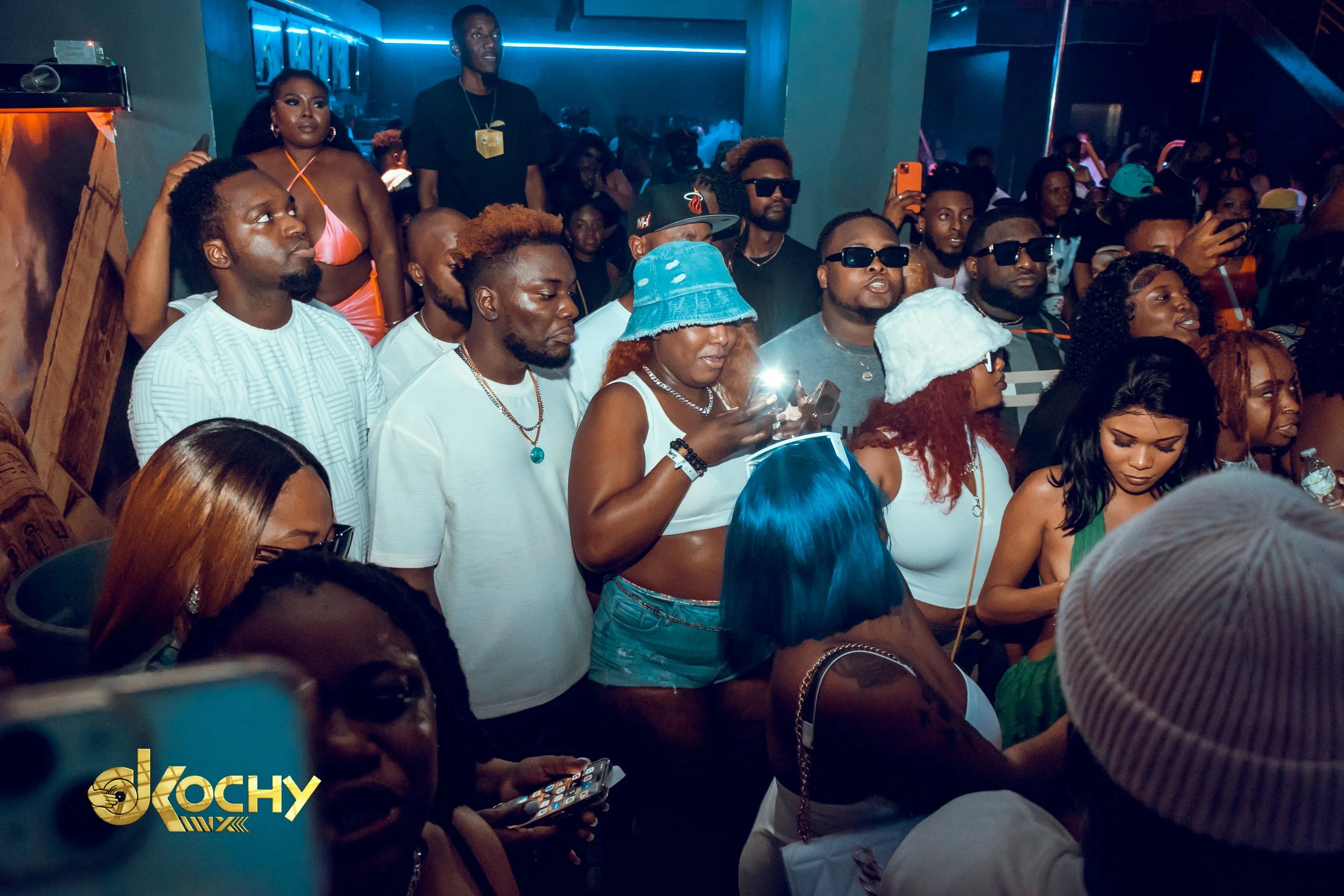 A crowd of people at a music event, with some wearing sunglasses, colorful hats, and casual clothing, enjoying the performance.