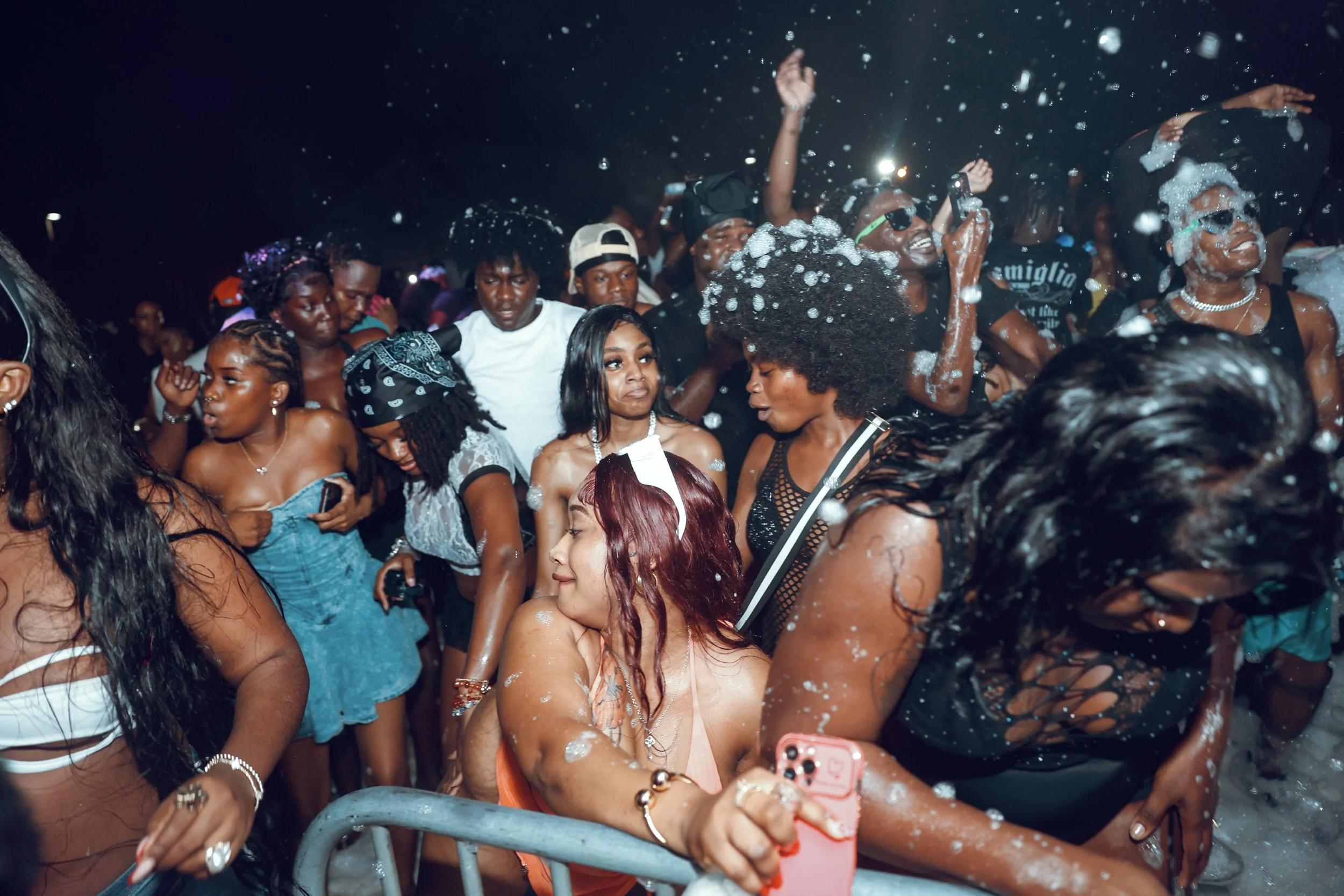 A crowd of people dancing and celebrating at a foam party at night, with foam foam foam and water splashing around.