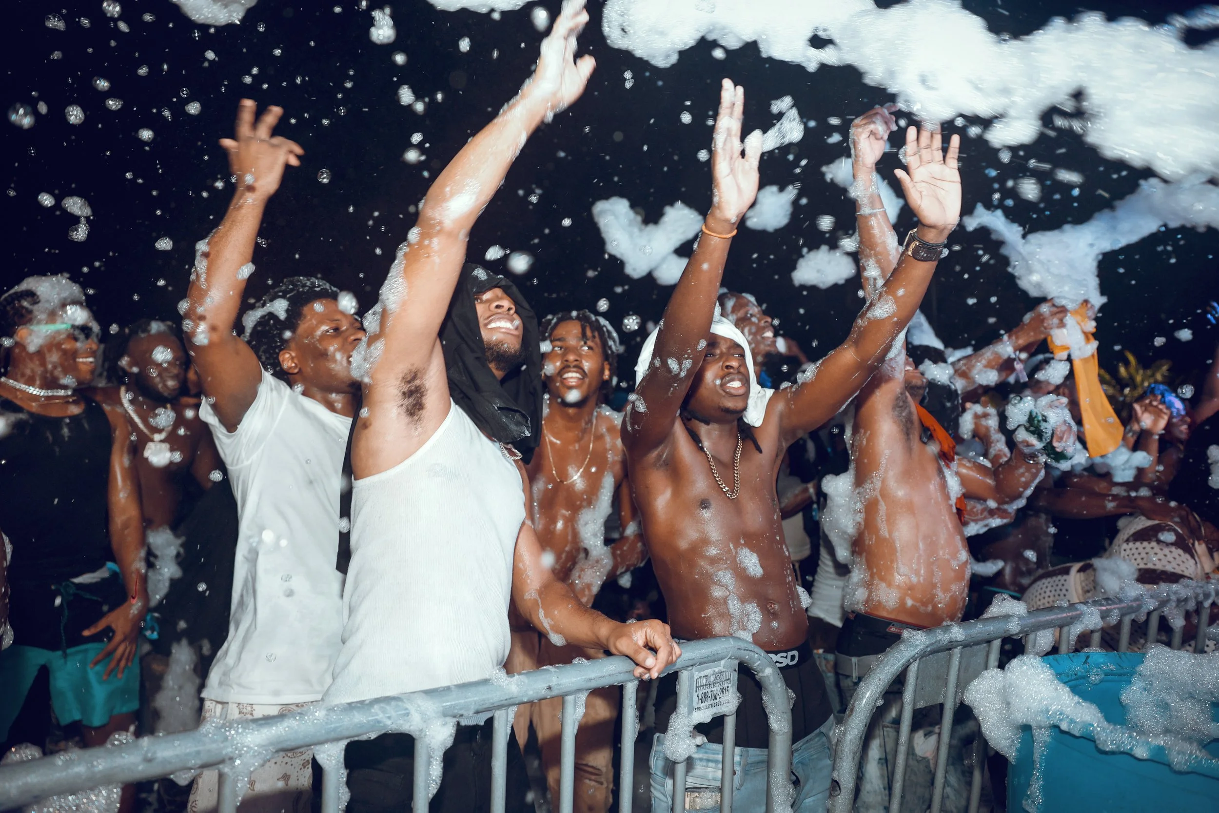People at a foam party celebrating with foam and water, raising their hands and enjoying themselves at night.
