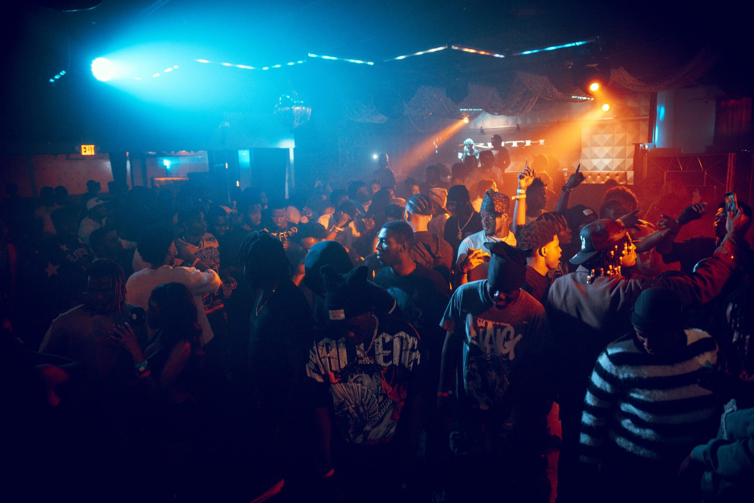 Crowd of people dancing and enjoying live music at a nightclub with colorful lighting and a DJ on stage.
