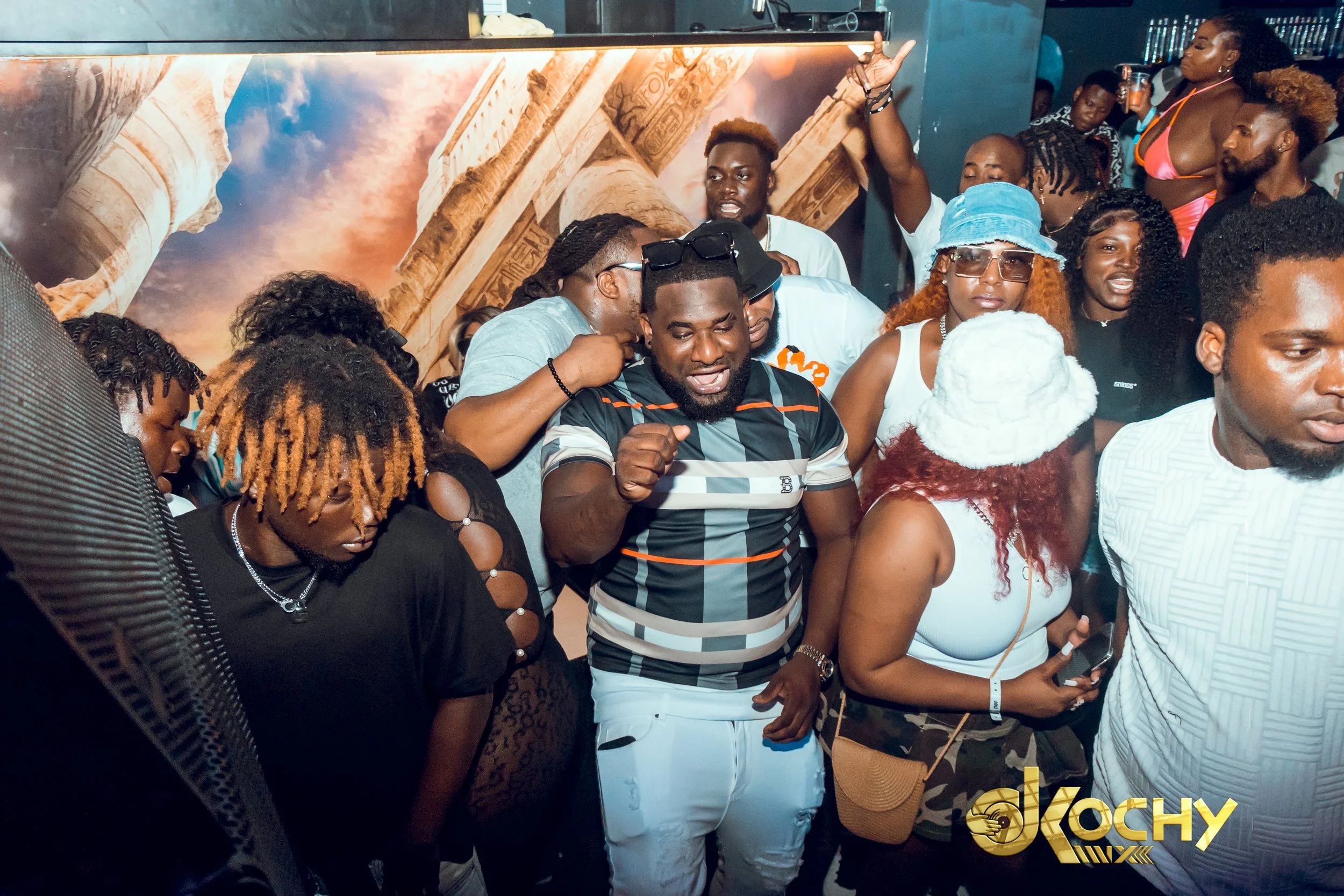 A group of people dancing and enjoying themselves at a nightclub or party, with some individuals raising their hands and others laughing.