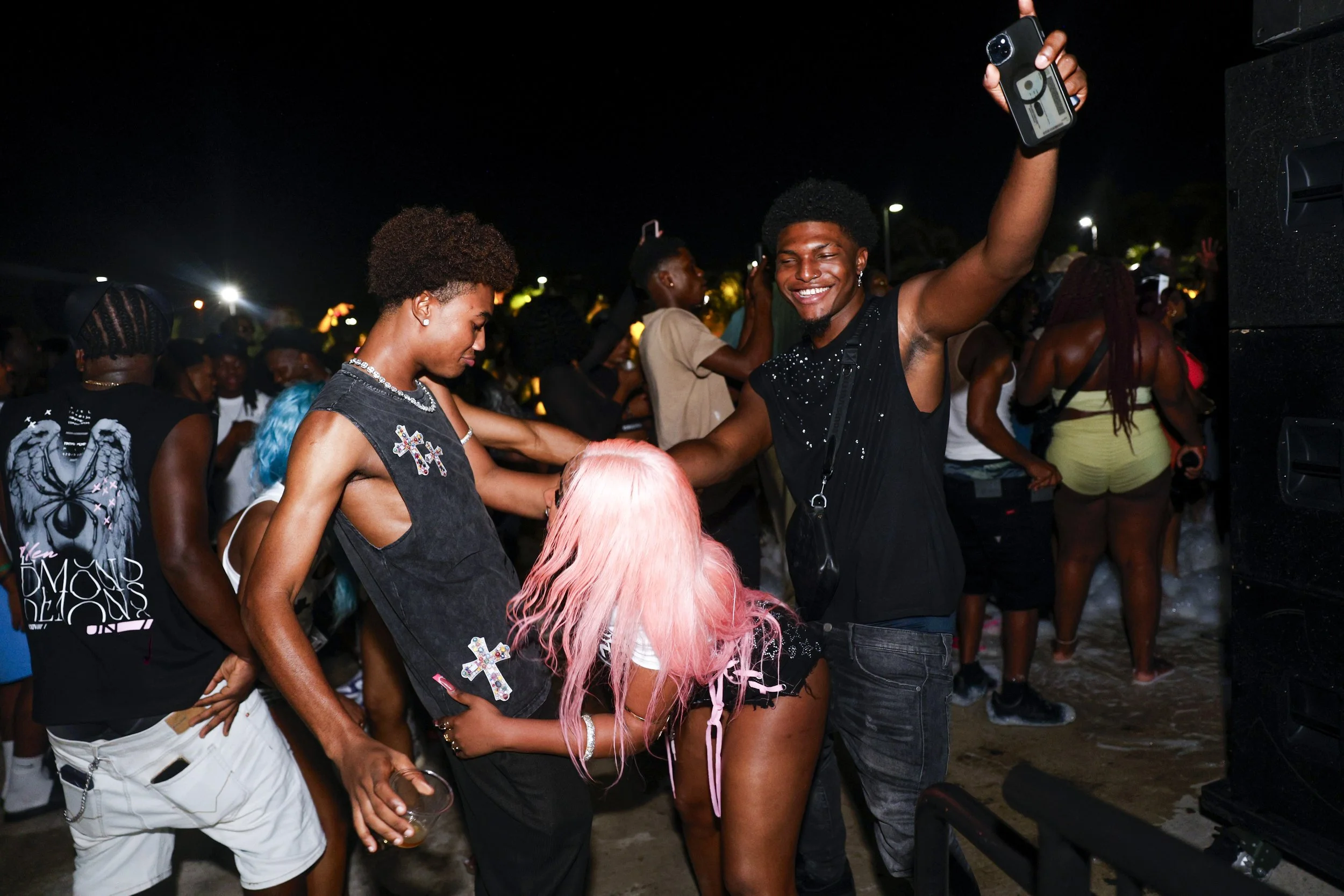 People dancing and enjoying themselves at an outdoor night event, with one person taking a selfie and others engaging in the festivities.
