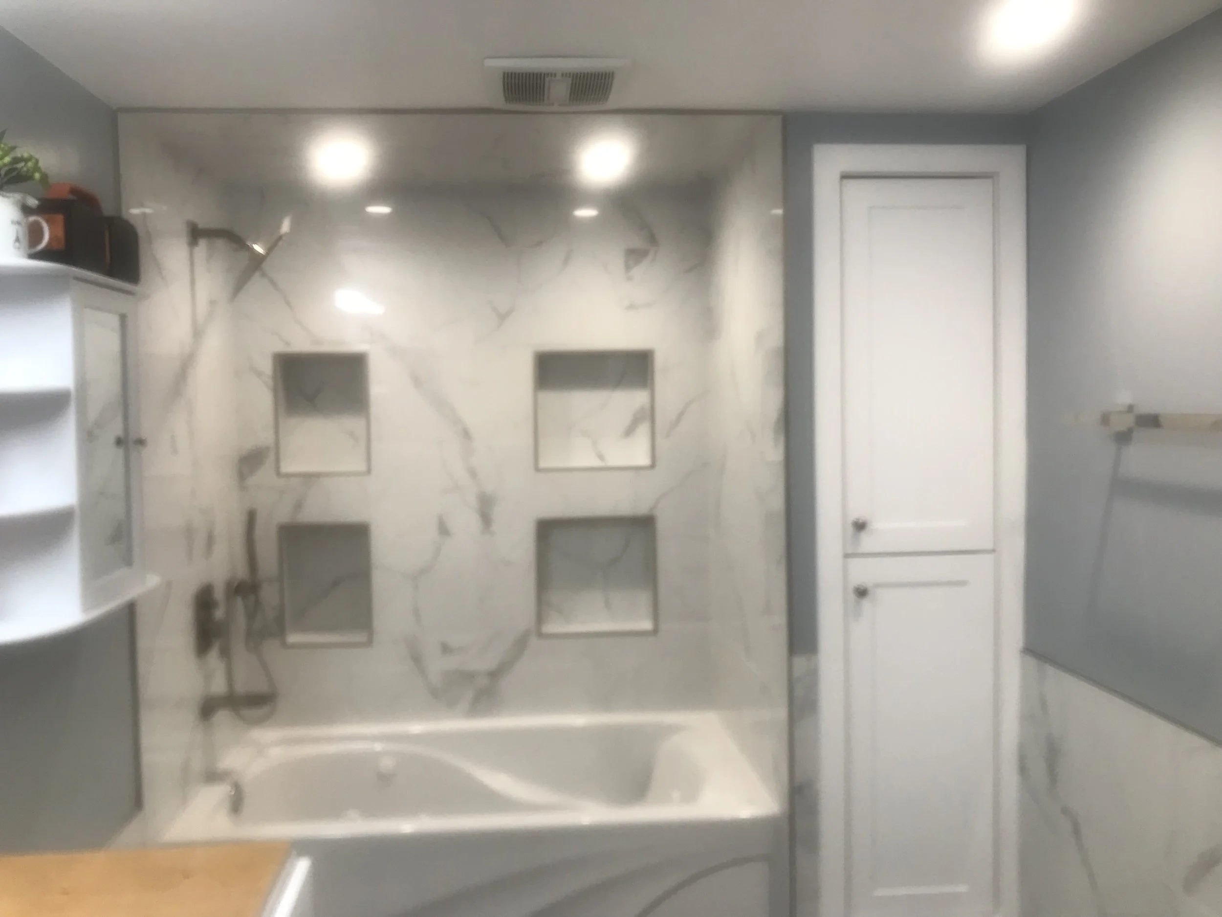 A bathroom with a marble accent wall, white cabinets, and a mirror.