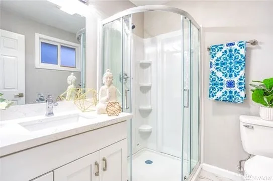 Bathroom with a glass shower enclosure, white vanity with decorative Buddha statues, a blue patterned towel hanging, and a green plant on the toilet tank.